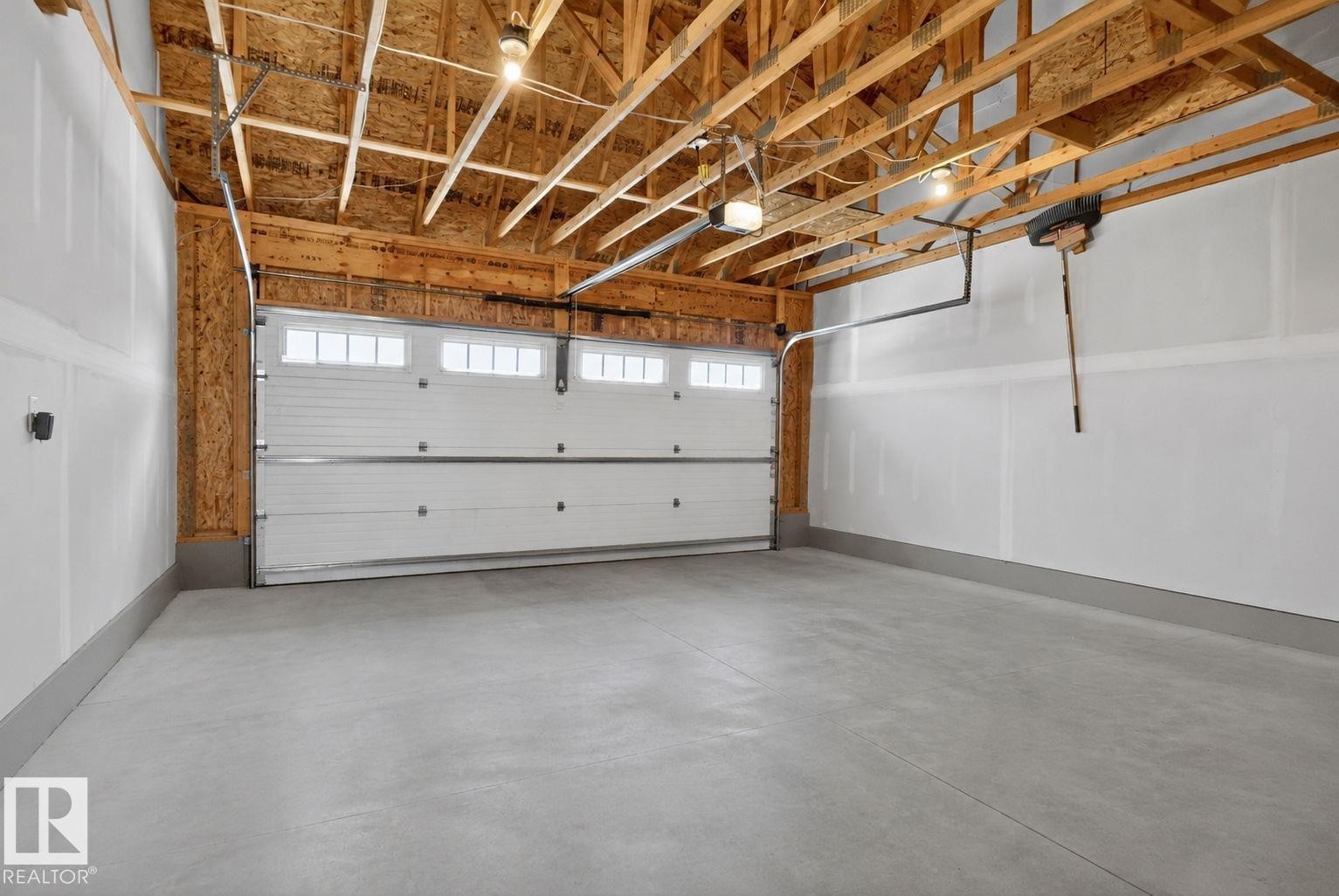 Spacious two-car garage featuring a concrete floor, exposed wood ceiling joists, and a white paneled garage door with upper window inserts - 319 Desrochers Boulevard Sw, Edmonton, AB - Indoor Photo Showing Garage