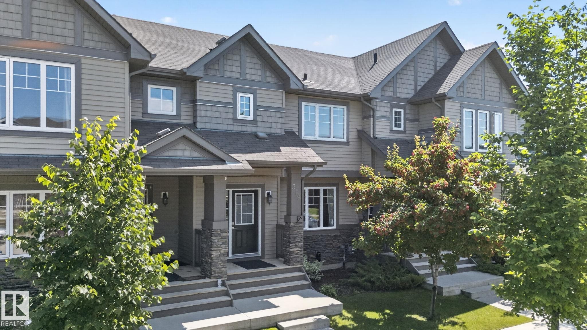 Townhome exterior featuring horizontal siding, stone accents, multiple gable roofs, white-framed windows, and covered entryways - 319 Desrochers Boulevard Sw, Edmonton, AB - Outdoor With Facade