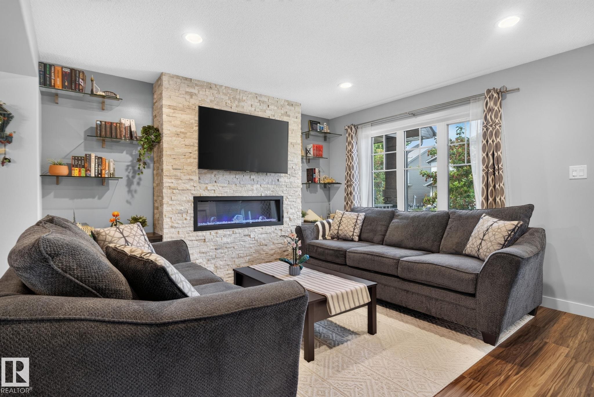 Living area featuring a floor-to-ceiling stacked stone fireplace with an integrated linear electric fireplace - 319 Desrochers Boulevard Sw, Edmonton, AB - Indoor Photo Showing Living Room With Fireplace