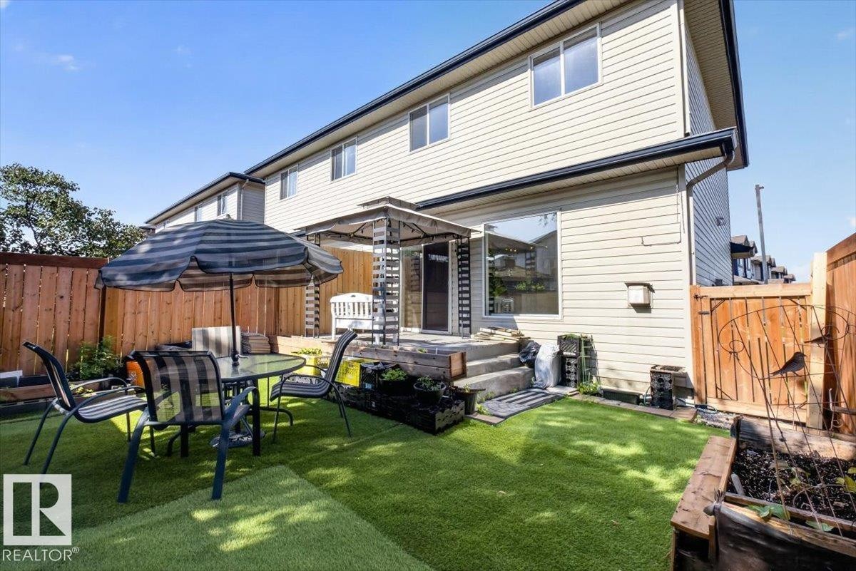 Fenced backyard featuring synthetic turf, a raised deck with a pergola, and a large ground-level window - #18 345 Kirkness Rd Nw, Edmonton, AB - Outdoor With Deck Patio Veranda