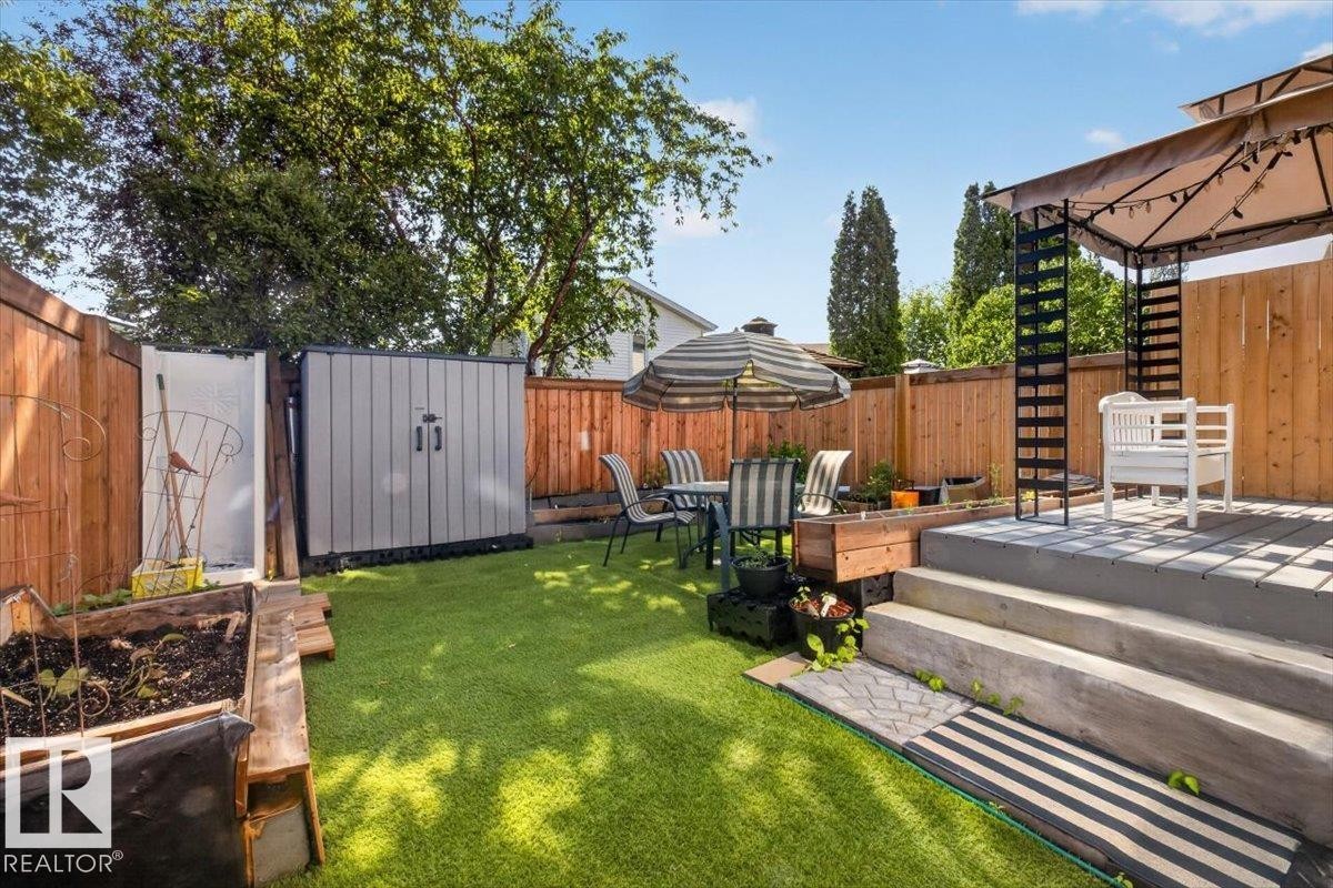 Fenced backyard featuring a tiered deck, artificial turf, raised garden beds, and a storage shed - #18 345 Kirkness Rd Nw, Edmonton, AB - Outdoor With Deck Patio Veranda