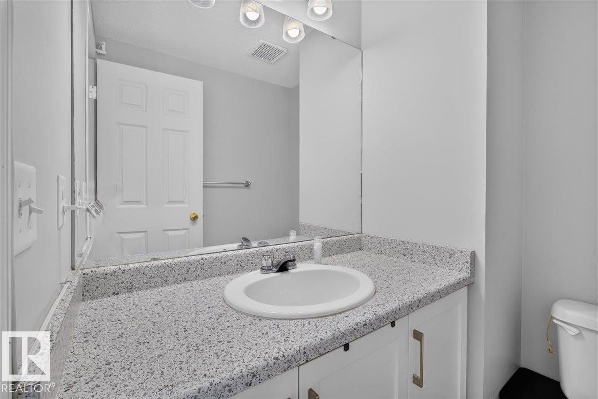 Vanity featuring a speckled countertop, integrated sink, and white cabinetry with brushed nickel hardware - #18 345 Kirkness Rd Nw, Edmonton, AB - Indoor Photo Showing Bathroom