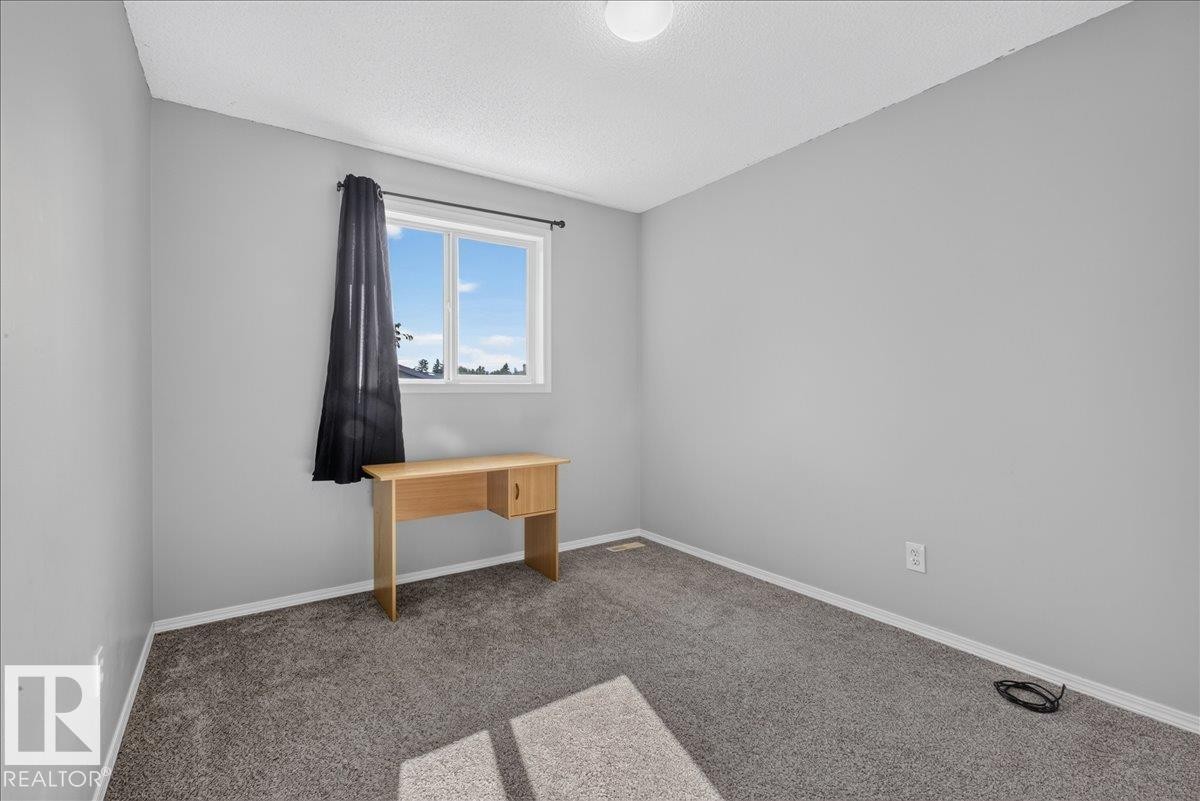 Light-filled room featuring neutral gray walls, textured gray carpeting, a single window with white trim, and a ceiling-mounted light fixture - #18 345 Kirkness Rd Nw, Edmonton, AB - Indoor Photo Showing Other Room