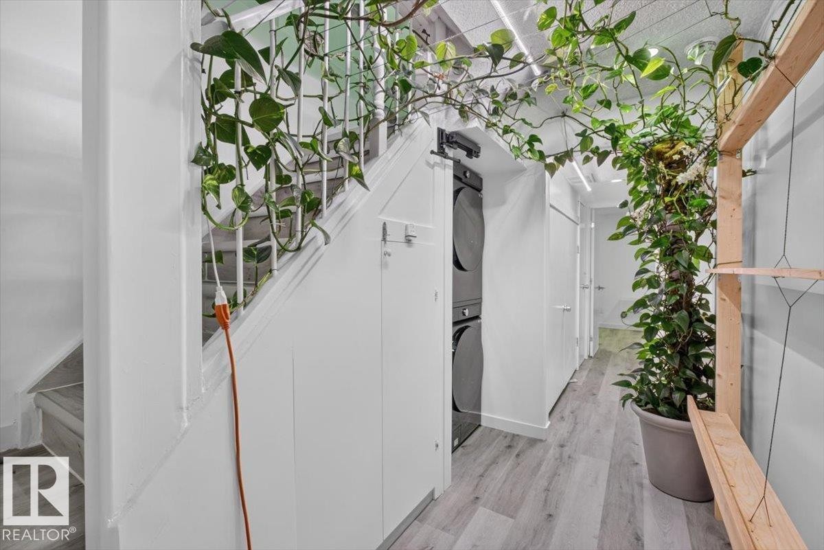 Integrated laundry station featuring stacked appliances, light wood-finish flooring, recessed lighting, and white paneled walls - #18 345 Kirkness Rd Nw, Edmonton, AB -
