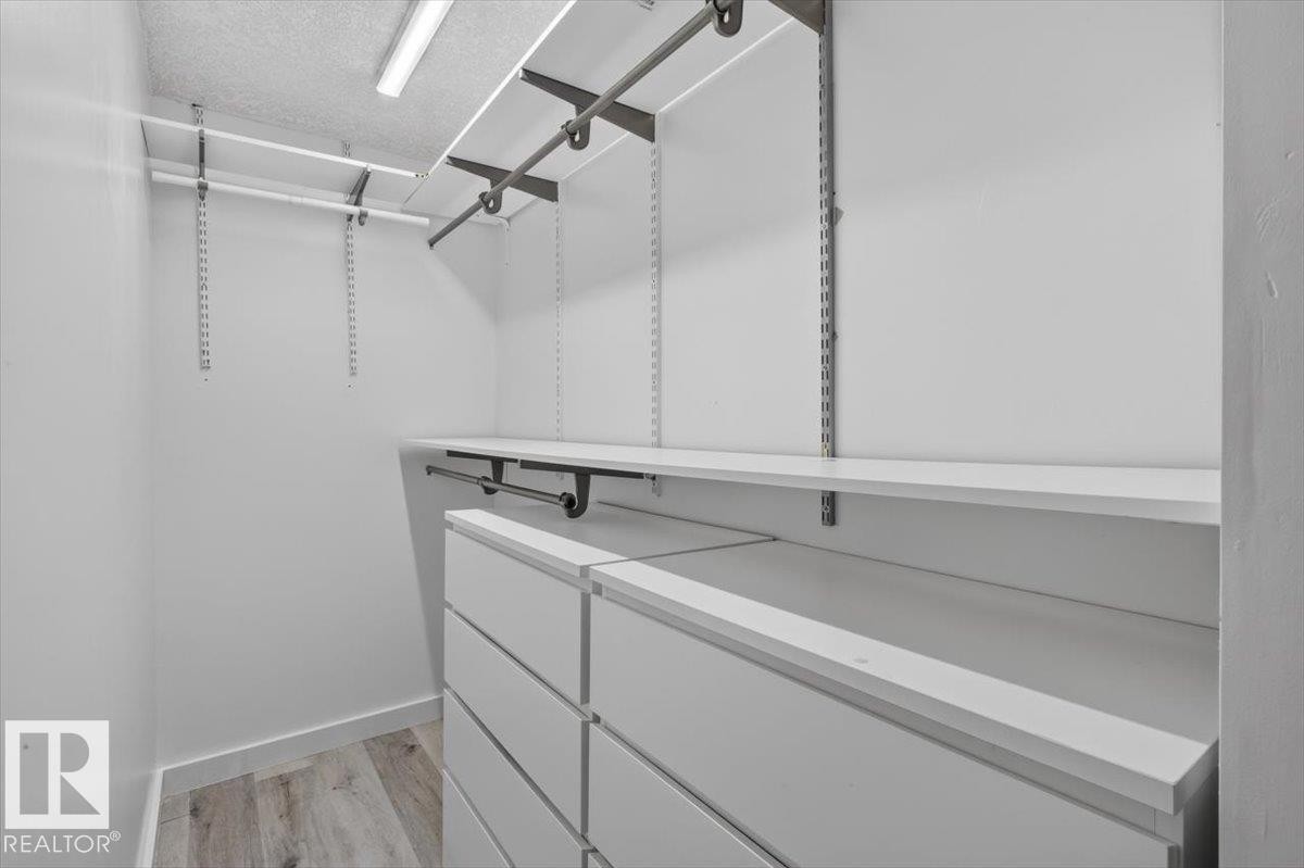 Walk-in closet featuring wood-finish flooring, modular shelving, integrated hanging rods, and built-in drawer units - #18 345 Kirkness Rd Nw, Edmonton, AB - Indoor With Storage