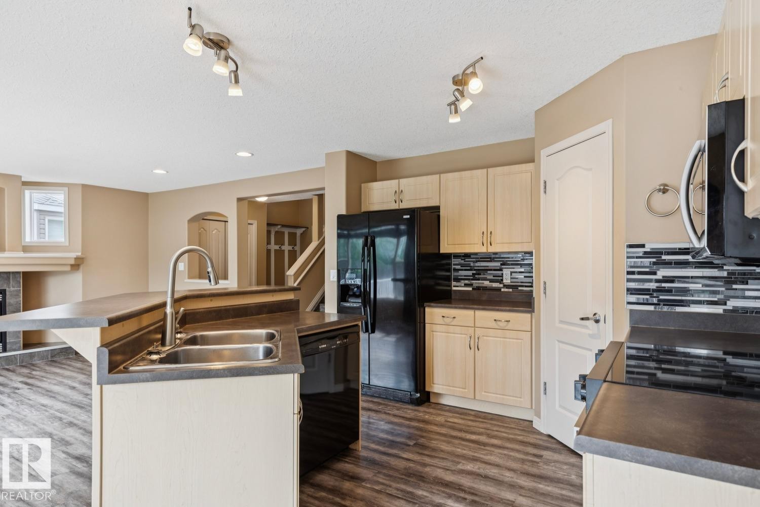 Kitchen featuring light wood cabinetry, dark countertops, and a mosaic tile backsplash - 16765 119 Street Nw, Edmonton, AB
