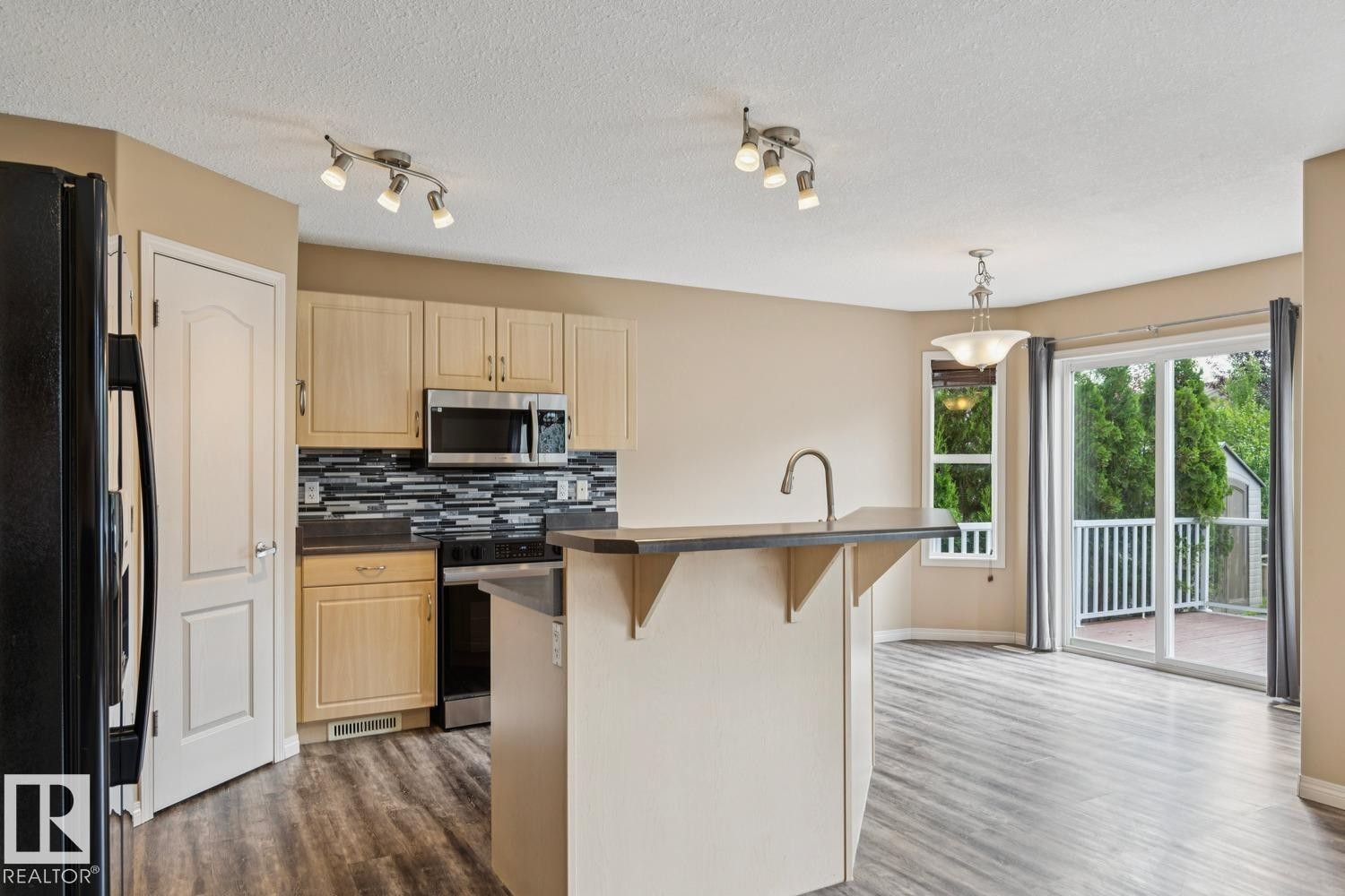 Kitchen featuring wood-finish cabinetry, stainless steel appliances, a multi-tone tile backsplash, and an island with a breakfast bar - 16765 119 Street Nw, Edmonton, AB