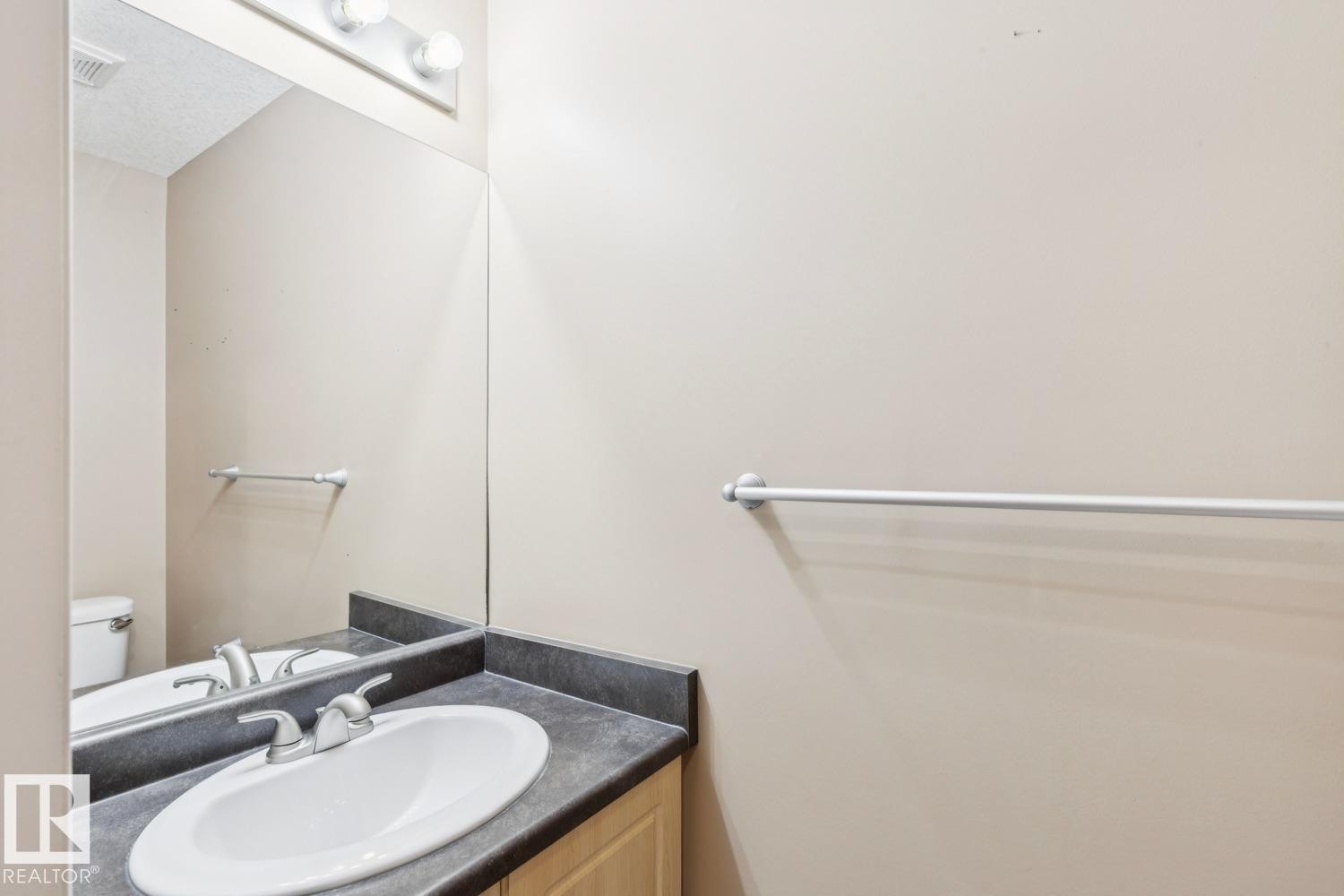 Bathroom vanity featuring a white oval sink, brushed nickel faucet, and dark countertop - 16765 119 Street Nw, Edmonton, AB