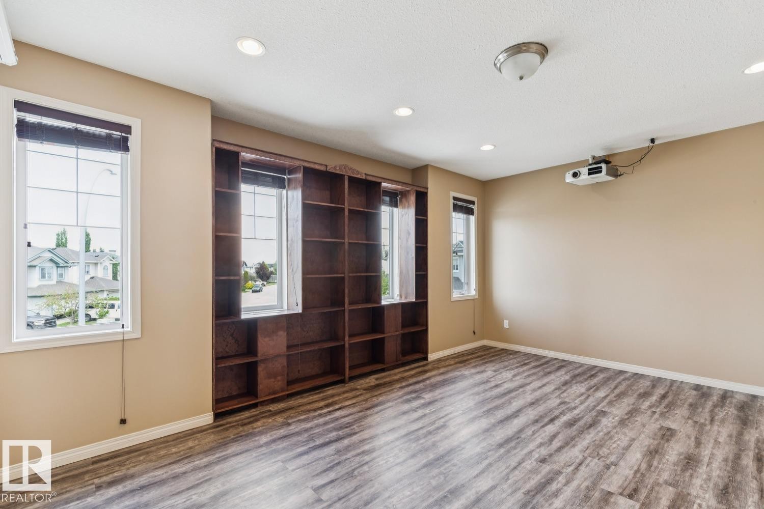 Spacious room featuring extensive built-in shelving, wood-finish flooring, multiple windows, recessed lighting, and a ceiling-mounted projector - 16765 119 Street Nw, Edmonton, AB