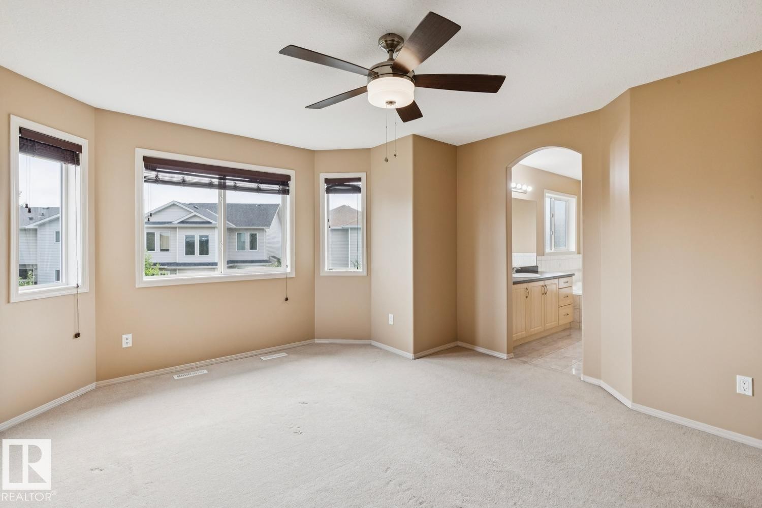 Spacious room featuring multiple windows with blinds, a ceiling fan with integrated lighting, and neutral carpeting - 16765 119 Street Nw, Edmonton, AB