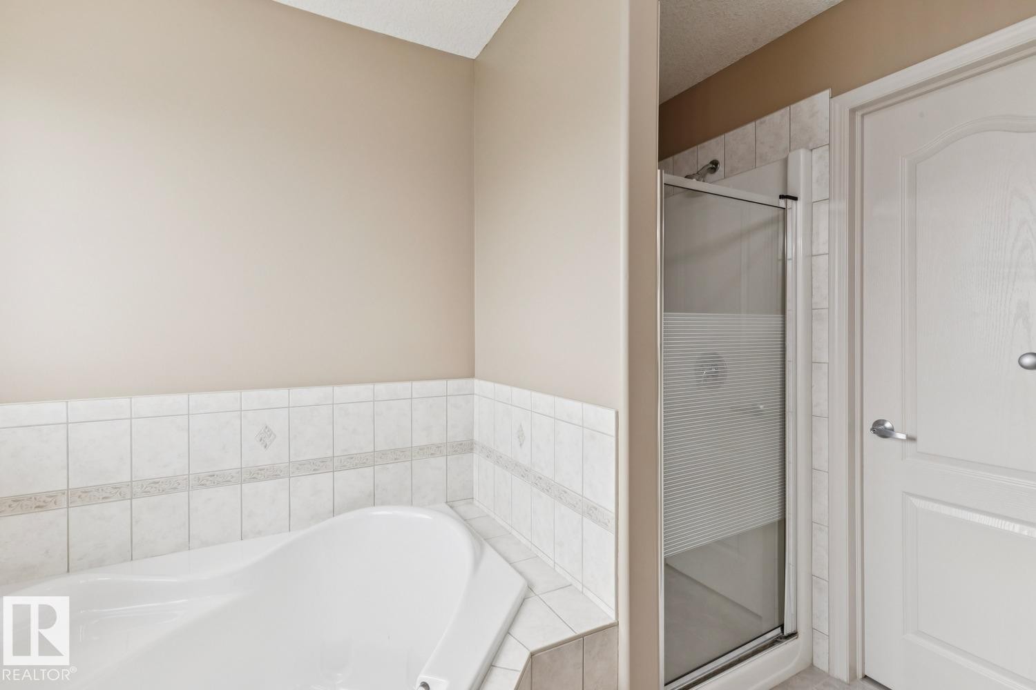 Corner soaking tub with white tile surround, glass-enclosed shower, and neutral wall tones - 16765 119 Street Nw, Edmonton, AB