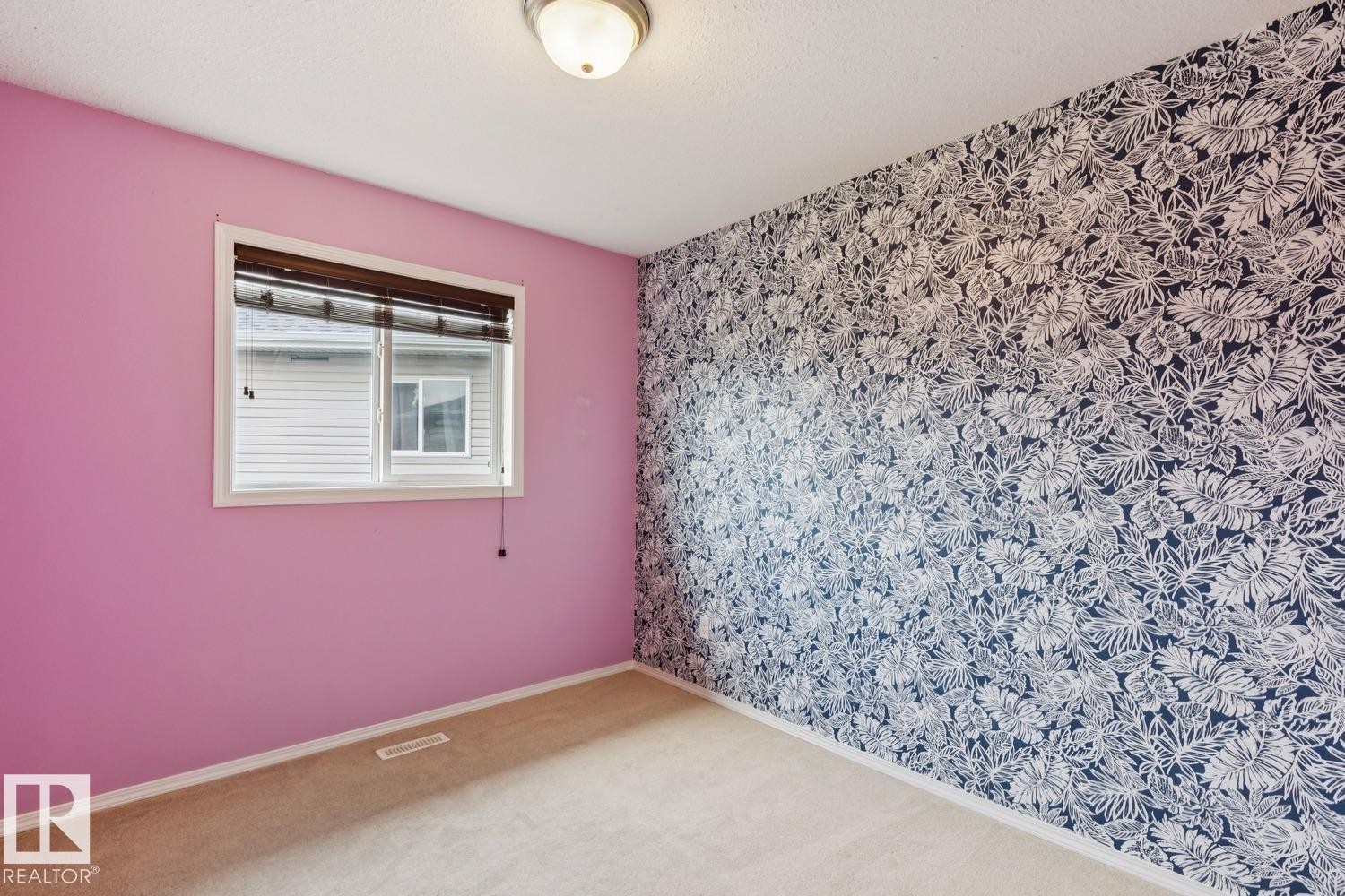 Room featuring a patterned accent wall, pink painted walls, a double-paned window with horizontal blinds, a ceiling-mounted light fixture, and neutral carpet flooring - 16765 119 Street Nw, Edmonton, AB
