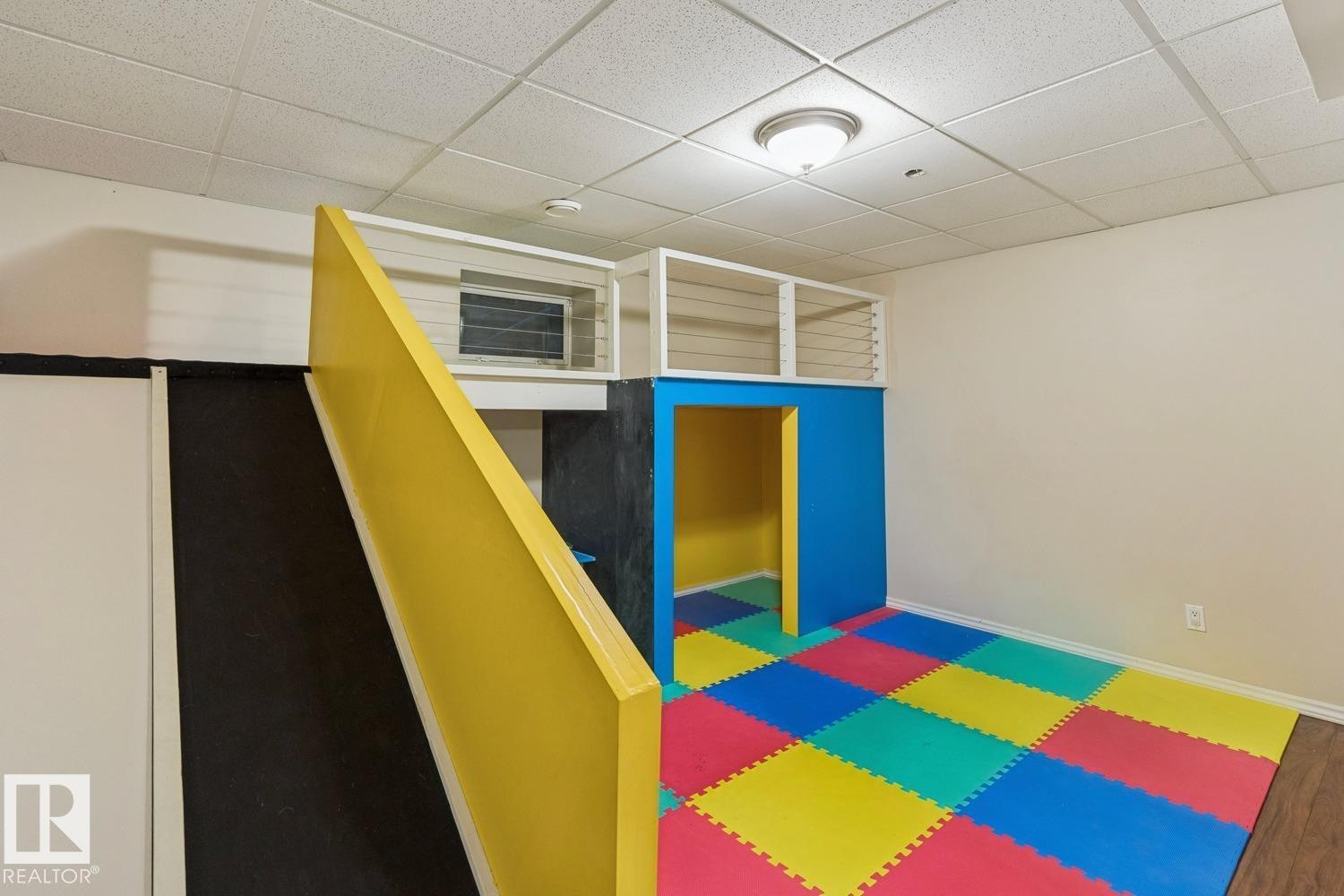 Recreational space featuring a colorful foam tile floor, a built-in play structure with a yellow ramp, and a white drop ceiling with recessed lighting - 16765 119 Street Nw, Edmonton, AB