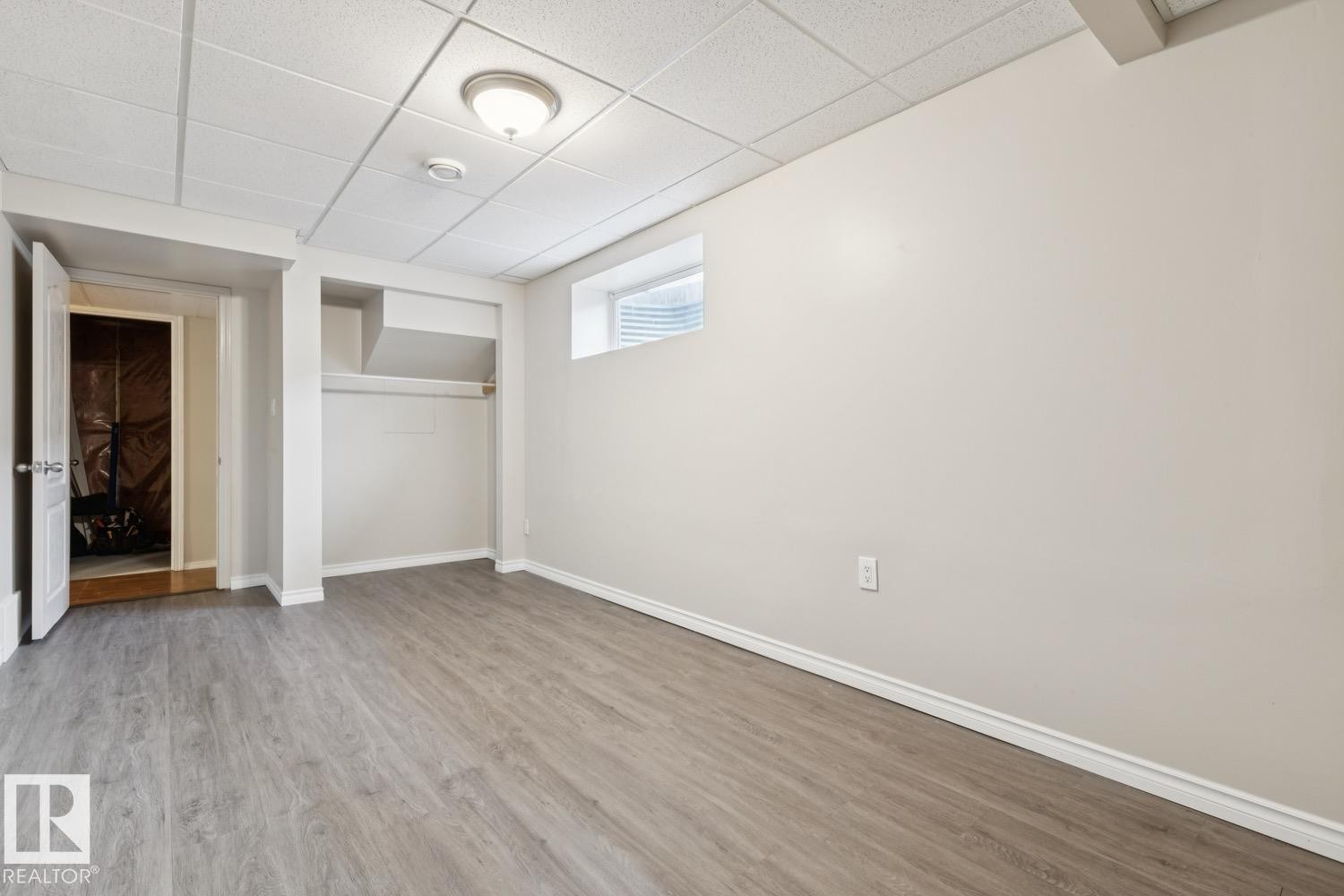 Spacious room featuring wood-finish flooring, light neutral wall paint, and a drop ceiling with recessed lighting - 16765 119 Street Nw, Edmonton, AB