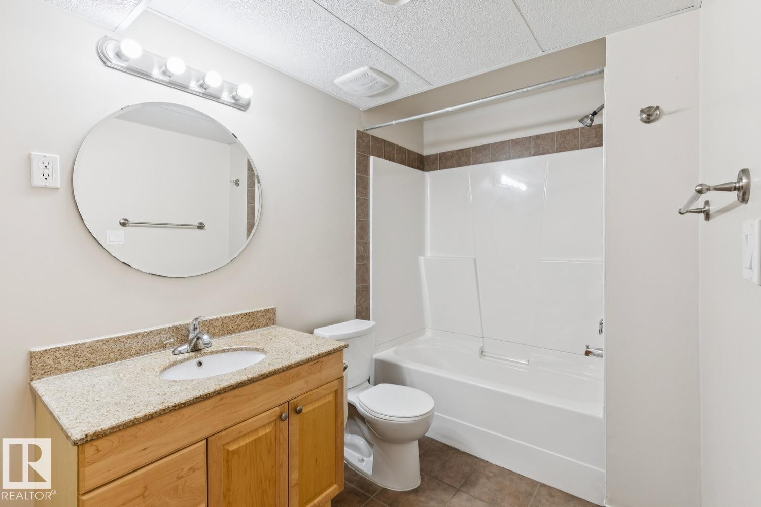 Bathroom featuring a light wood-finish vanity with a granite-style countertop, an oval-shaped sink, and a circular wall mirror - 16765 119 Street Nw, Edmonton, AB