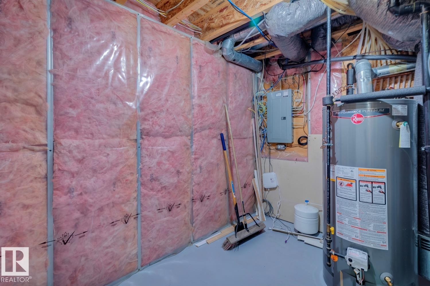Utility area featuring a Rheem water heater, electrical panel, exposed ceiling joists, and insulated wall framing - 16765 119 Street Nw, Edmonton, AB