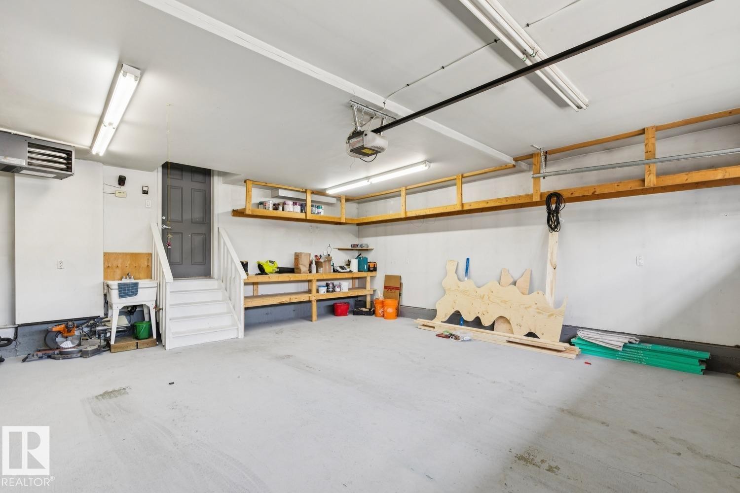 Spacious garage featuring a utility sink, built-in shelving, concrete flooring, overhead lighting, and an interior access door - 16765 119 Street Nw, Edmonton, AB