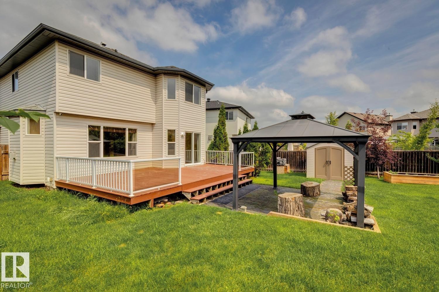 Expansive backyard featuring a multi-level deck with clear panel railing, a dedicated patio space with gazebo, and a storage shed - 16765 119 Street Nw, Edmonton, AB