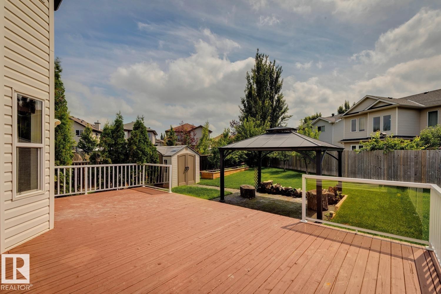 Spacious red-stained wood deck featuring white railings and a partial glass barrier - 16765 119 Street Nw, Edmonton, AB