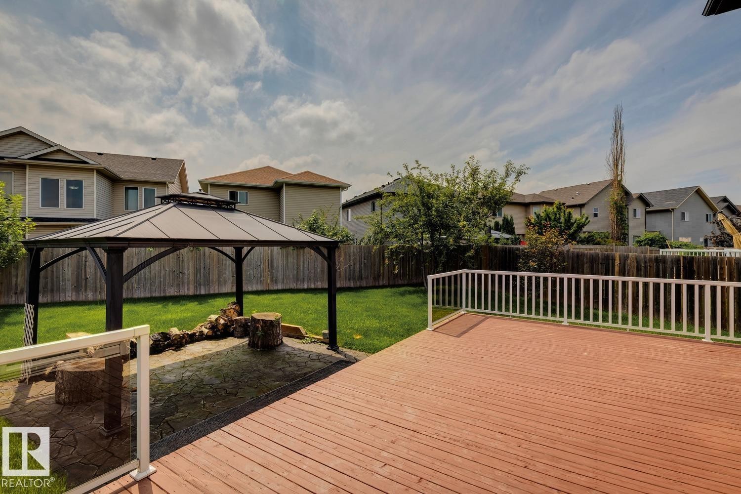 Expansive backyard featuring a spacious wood deck with white railings, a covered gazebo, and a stamped concrete patio area - 16765 119 Street Nw, Edmonton, AB