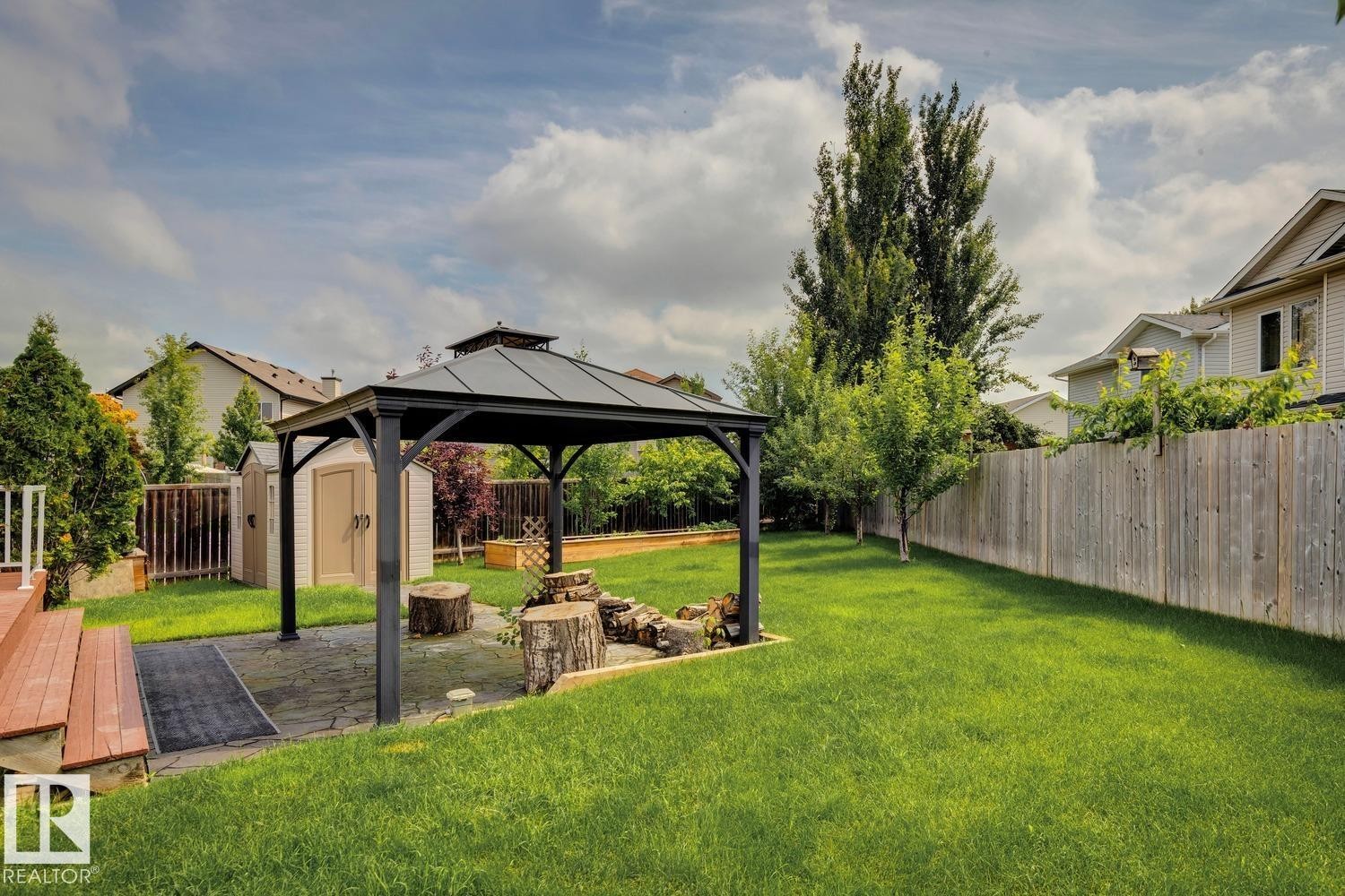 Expansive backyard featuring a central gazebo with a paved area, a fire pit with log seating, a storage shed, and a wooden fence - 16765 119 Street Nw, Edmonton, AB