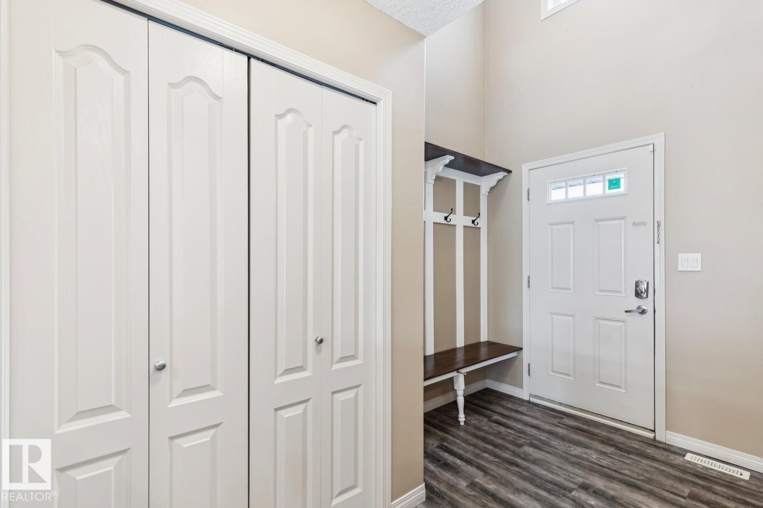 Entryway with wood-finish flooring, a built-in bench with hooks, a white panel door with transom windows, and white bifold closet doors - 16765 119 Street Nw, Edmonton, AB