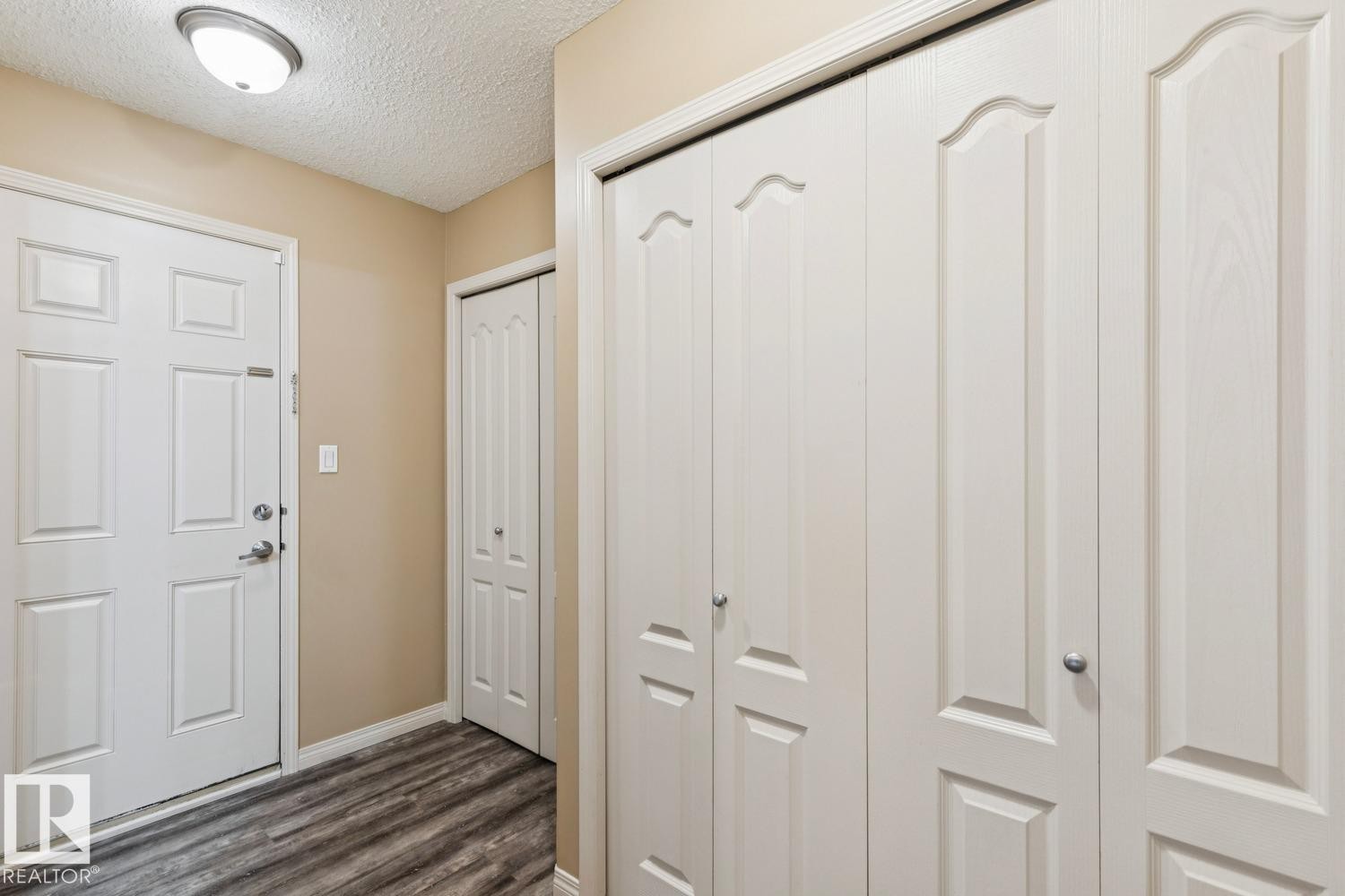 Entryway featuring wood-finish flooring, a flush mount ceiling light, and ample storage with multiple paneled bi-fold doors - 16765 119 Street Nw, Edmonton, AB