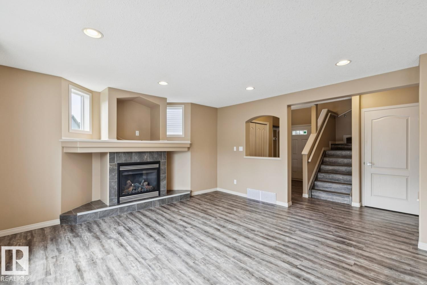 Spacious living area featuring wood-finish flooring, a tiled fireplace with mantel, recessed lighting, and ample natural light from multiple windows - 16765 119 Street Nw, Edmonton, AB