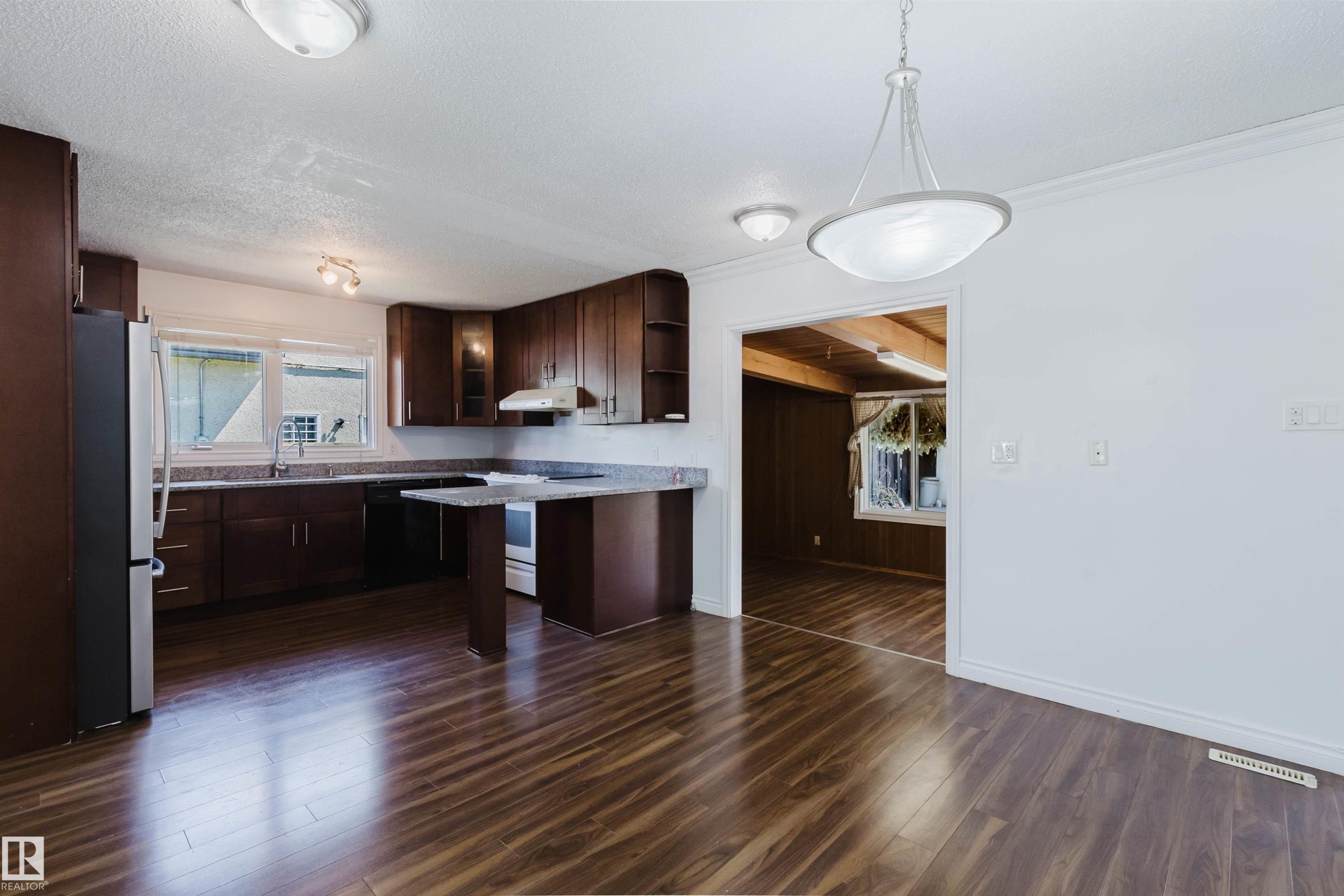 Spacious kitchen featuring dark wood cabinetry, light-toned countertops, and wood-finish flooring - 11115 39A Avenue Nw, Edmonton, AB - Indoor Photo Showing Kitchen