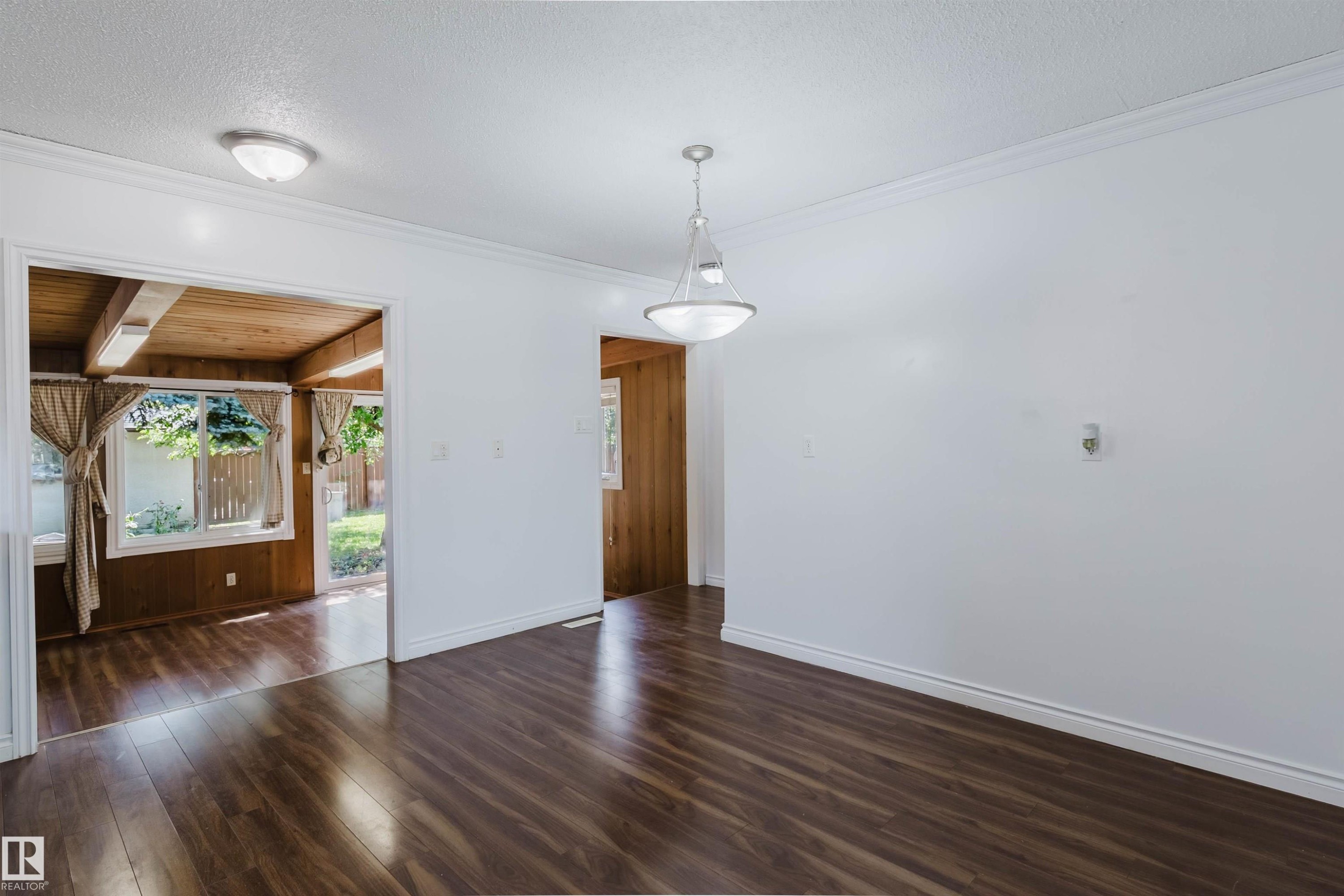 Spacious room featuring wood-finish flooring, white walls, and a contemporary pendant light fixture - 11115 39A Avenue Nw, Edmonton, AB - Indoor Photo Showing Other Room
