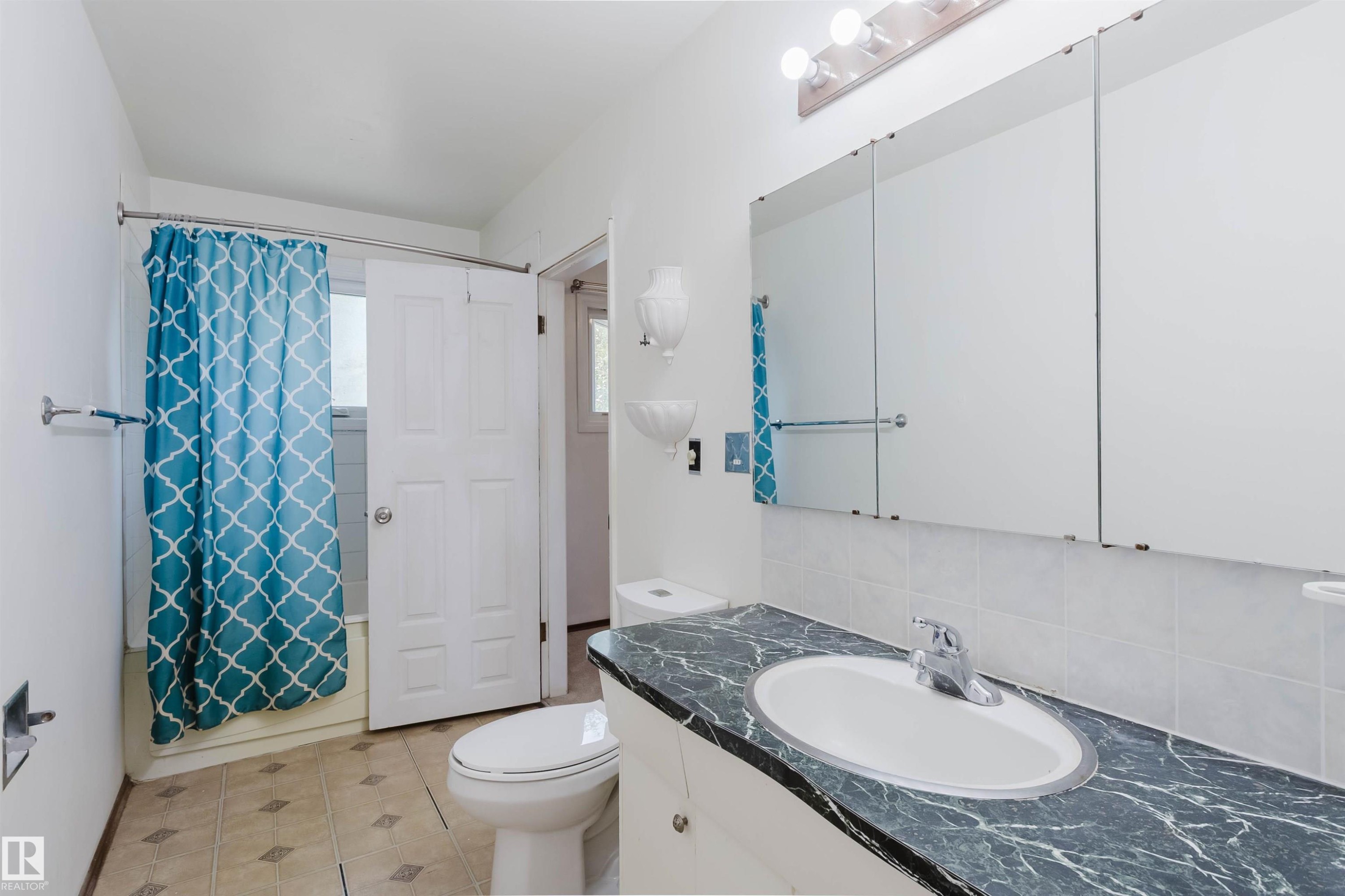 Bathroom featuring a gray marbled vanity countertop with an undermount sink, a large wall-mounted mirror, ceramic tile flooring, and a shower-over-tub combination with a curved shower rod - 11115 39A Avenue Nw, Edmonton, AB - Indoor Photo Showing Bathroom
