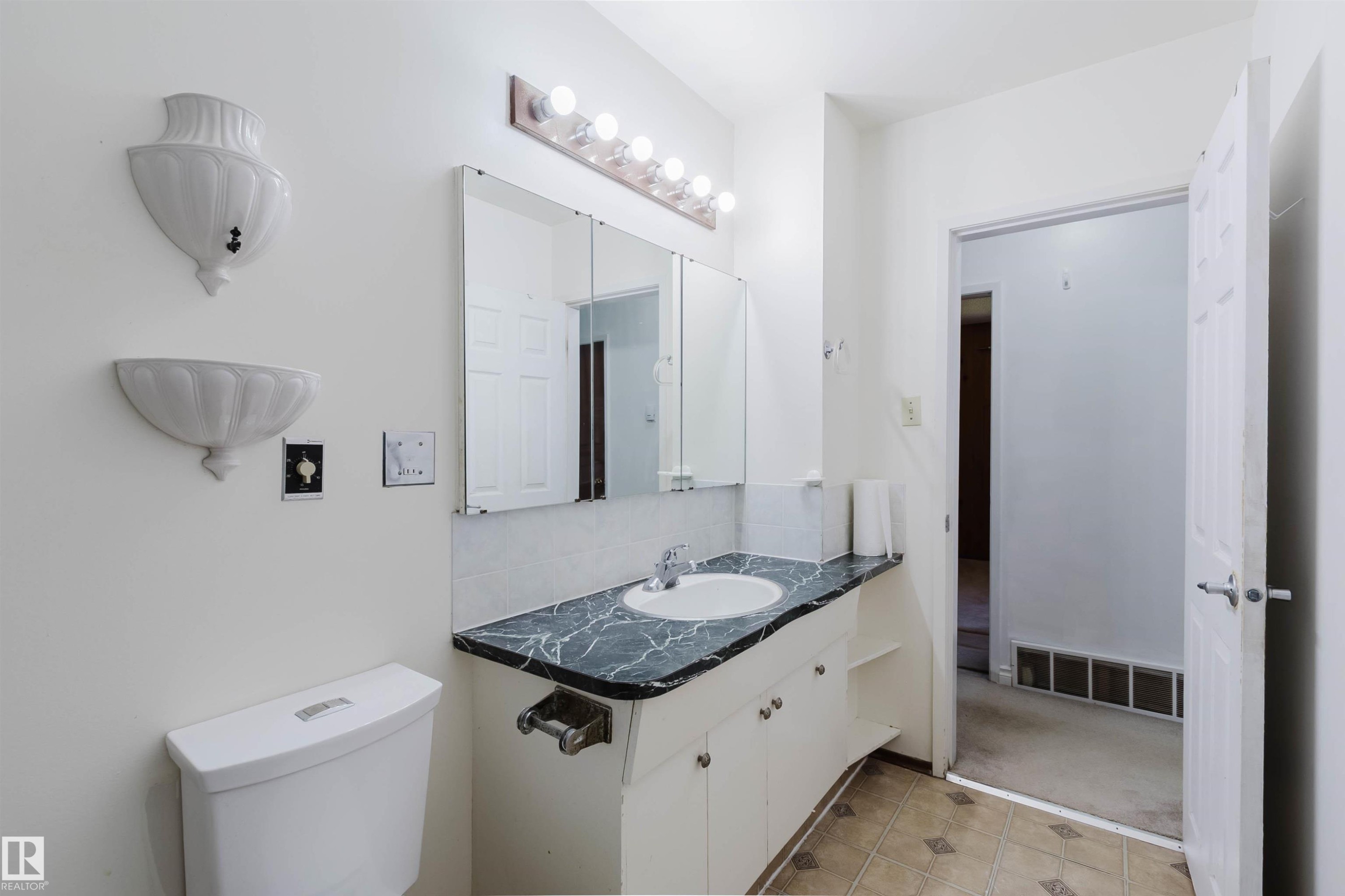 Bathroom featuring a white toilet, white vanity with integrated sink, patterned countertop, and mirrored medicine cabinet - 11115 39A Avenue Nw, Edmonton, AB - Indoor Photo Showing Bathroom
