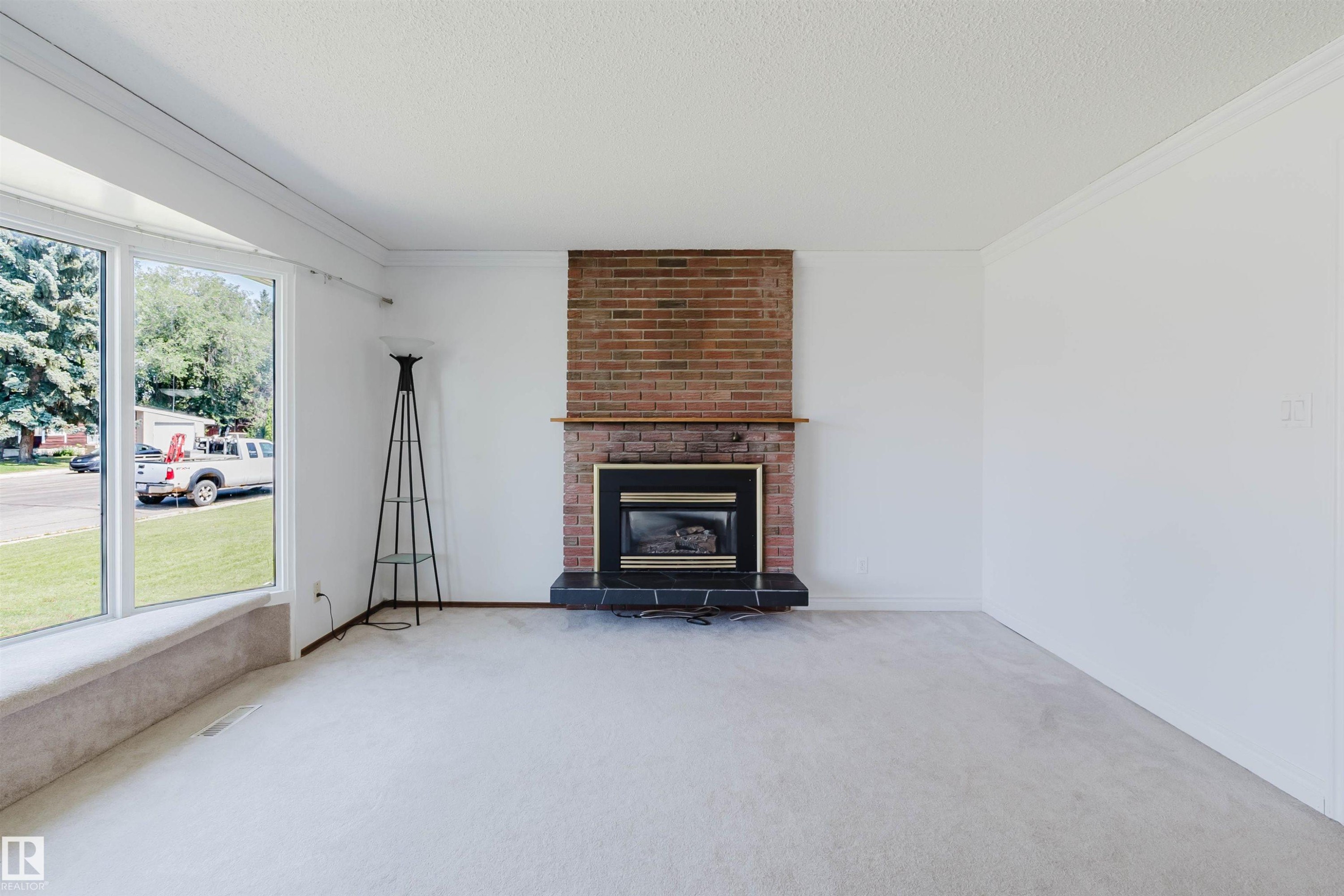 Living area with bay window, brick fireplace with mantel, black hearth, and light-toned carpeting - 11115 39A Avenue Nw, Edmonton, AB - Indoor Photo Showing Living Room With Fireplace