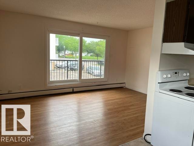 Spacious room featuring wood-finish flooring, a large sliding glass door, and a private balcony with metal railings - #205 10740 105 St Nw, Edmonton, AB - Indoor Photo Showing Kitchen
