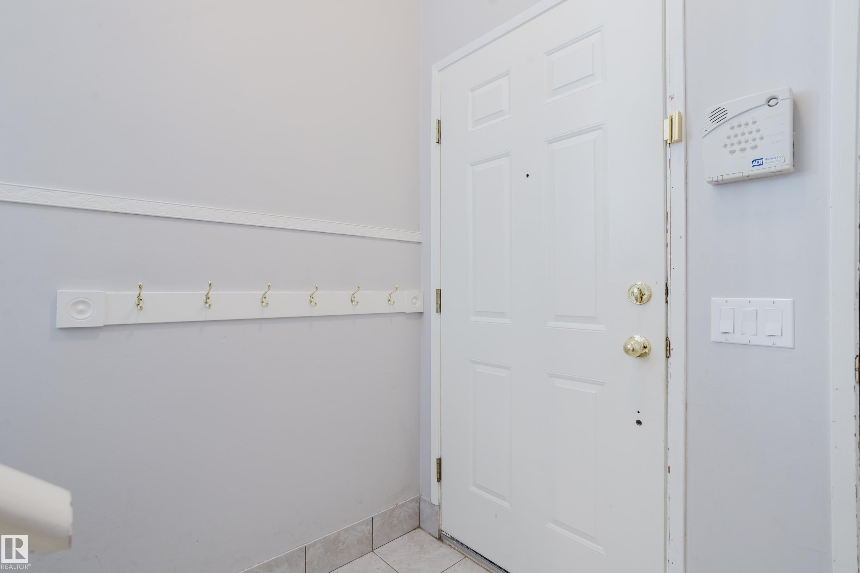 Entryway featuring a paneled door with brass hardware, tile flooring, a wall-mounted coat rack with brass hooks, and an alarm system keypad - 337 Pearson Crescent Nw, Edmonton, AB - Indoor Photo Showing Other Room