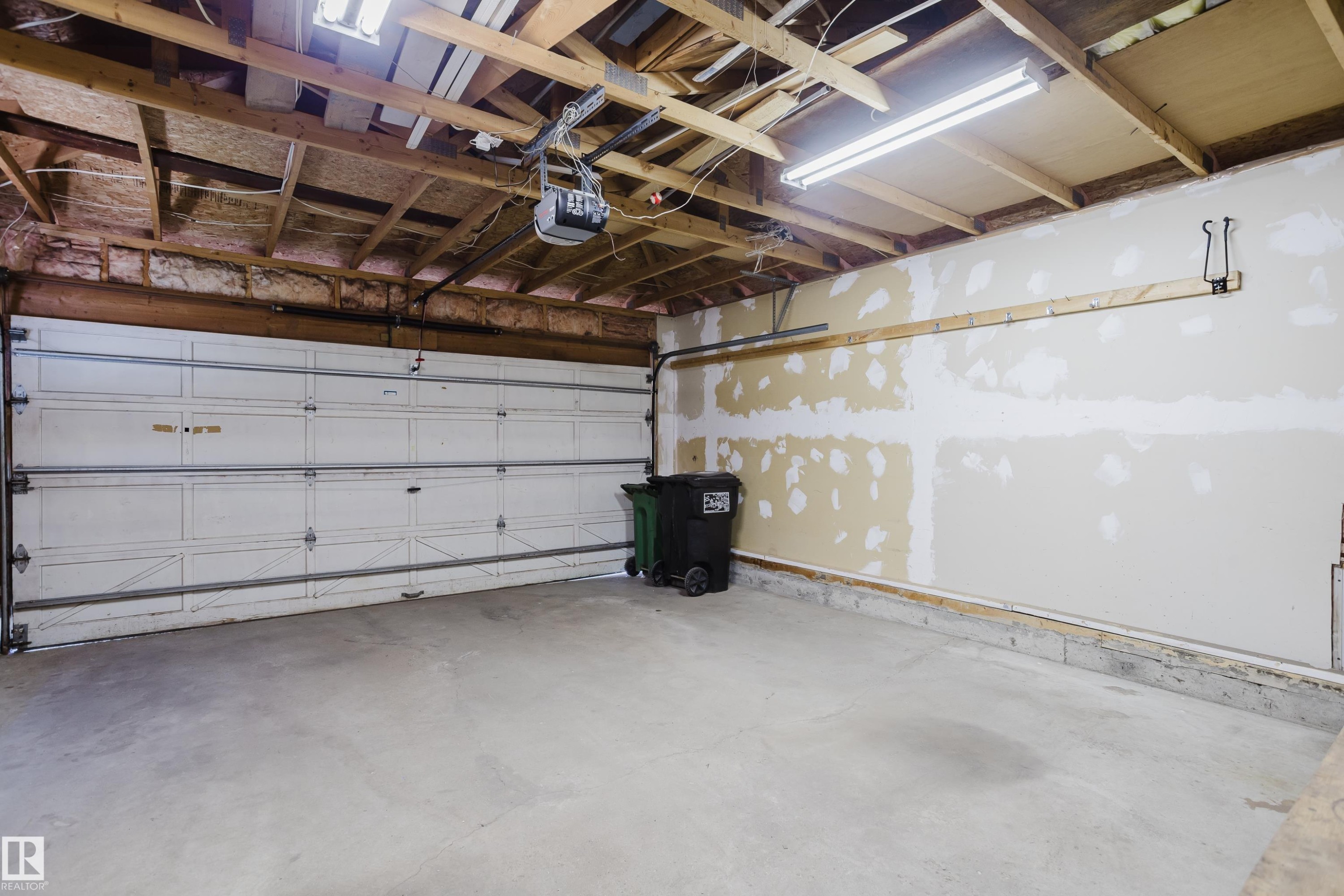 Spacious garage featuring a concrete floor, overhead fluorescent lighting, exposed wood ceiling joists, and a sectional garage door with an automatic opener - 337 Pearson Crescent Nw, Edmonton, AB - Indoor Photo Showing Garage