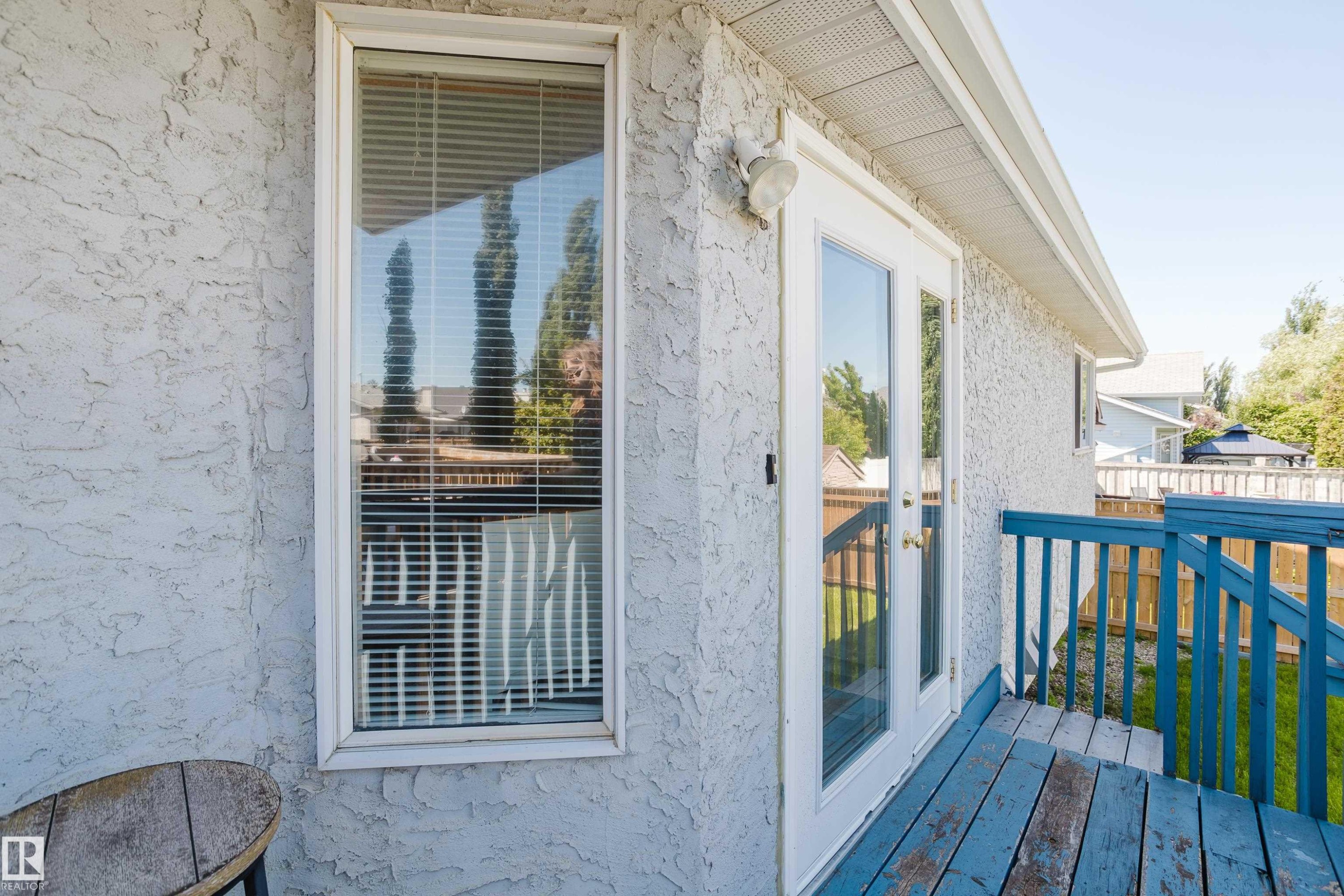 Textured exterior wall featuring a window with blinds, double glass-paneled doors, and an outdoor deck with blue railing - 337 Pearson Crescent Nw, Edmonton, AB - Outdoor With Exterior