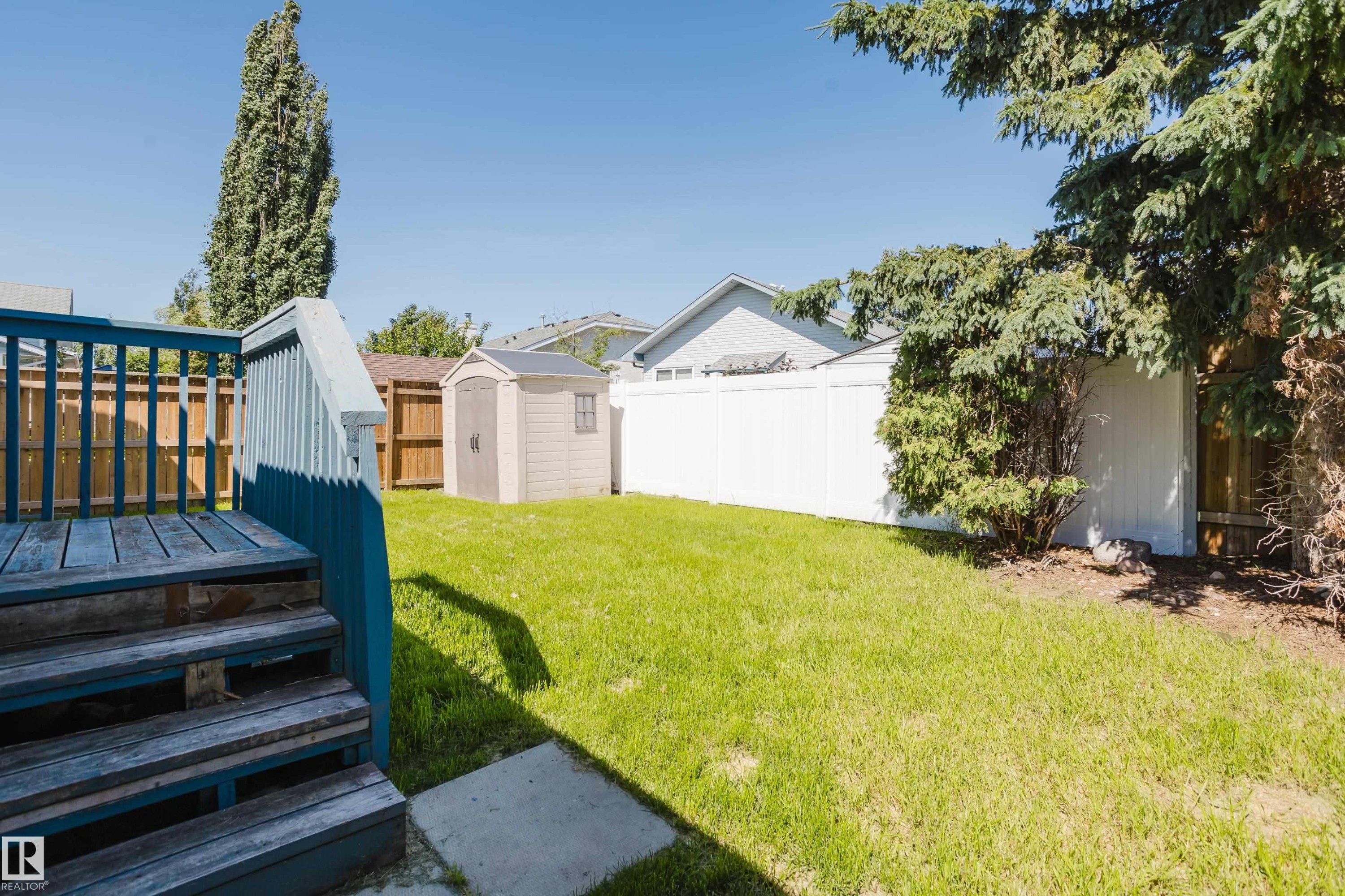Spacious backyard featuring a green lawn, a blue-painted wood deck with stairs, and a light-colored storage shed - 337 Pearson Crescent Nw, Edmonton, AB - Outdoor
