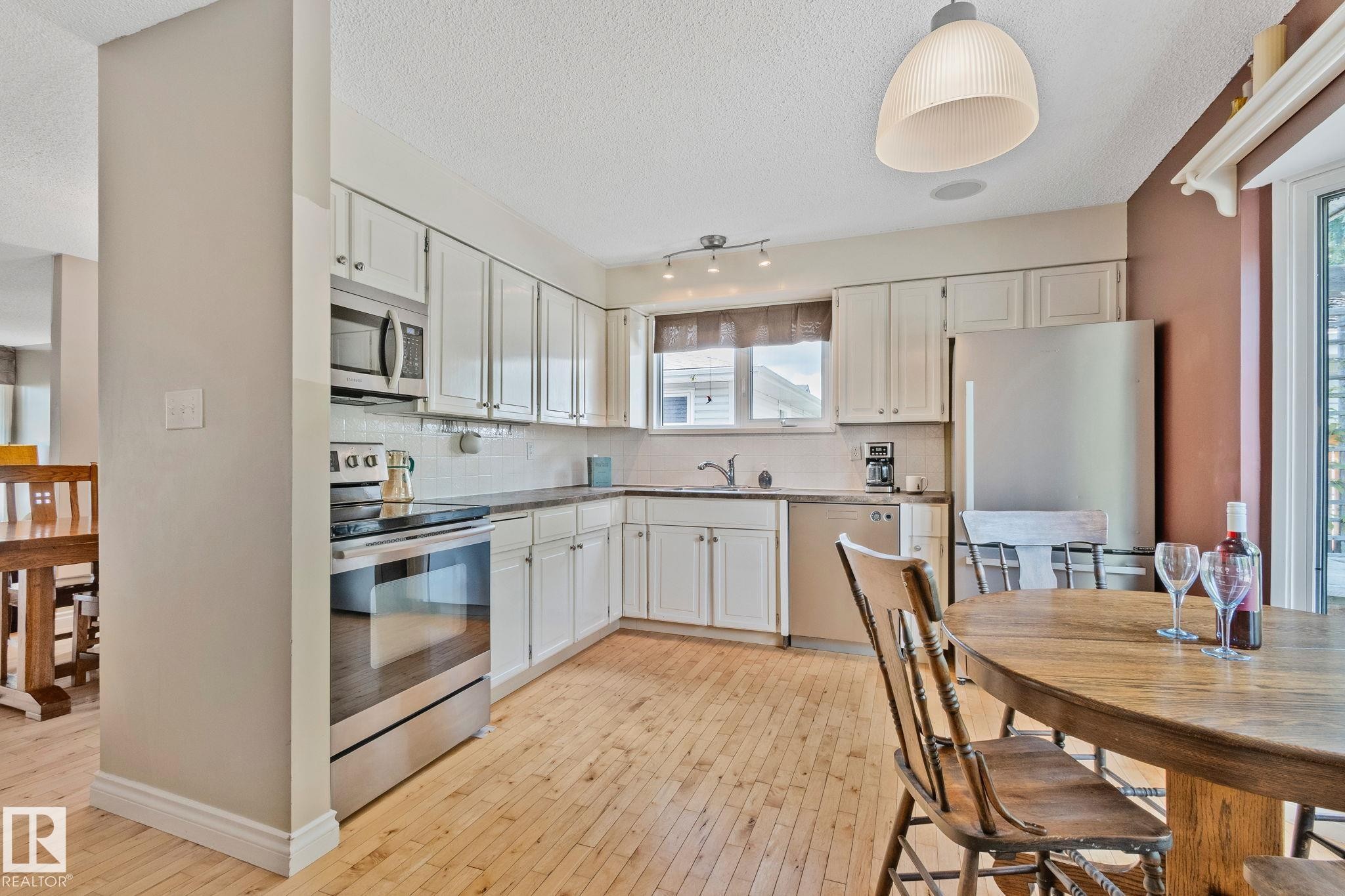 Kitchen featuring light wood-finish flooring, white cabinetry, stainless steel appliances, and a tile backsplash - 7306 21 Avenue Nw, Edmonton, AB - Indoor