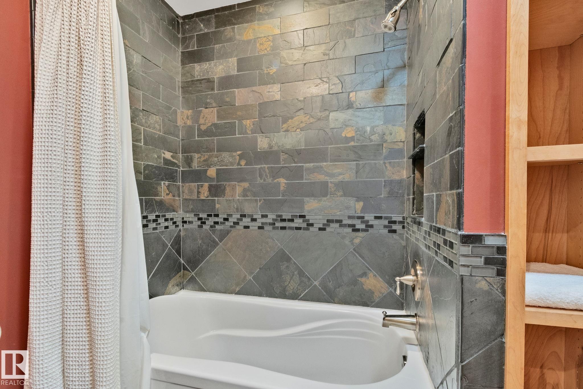 Bathtub and shower combination featuring natural stone tile walls with a decorative mosaic accent band - 7306 21 Avenue Nw, Edmonton, AB - Indoor Photo Showing Bathroom