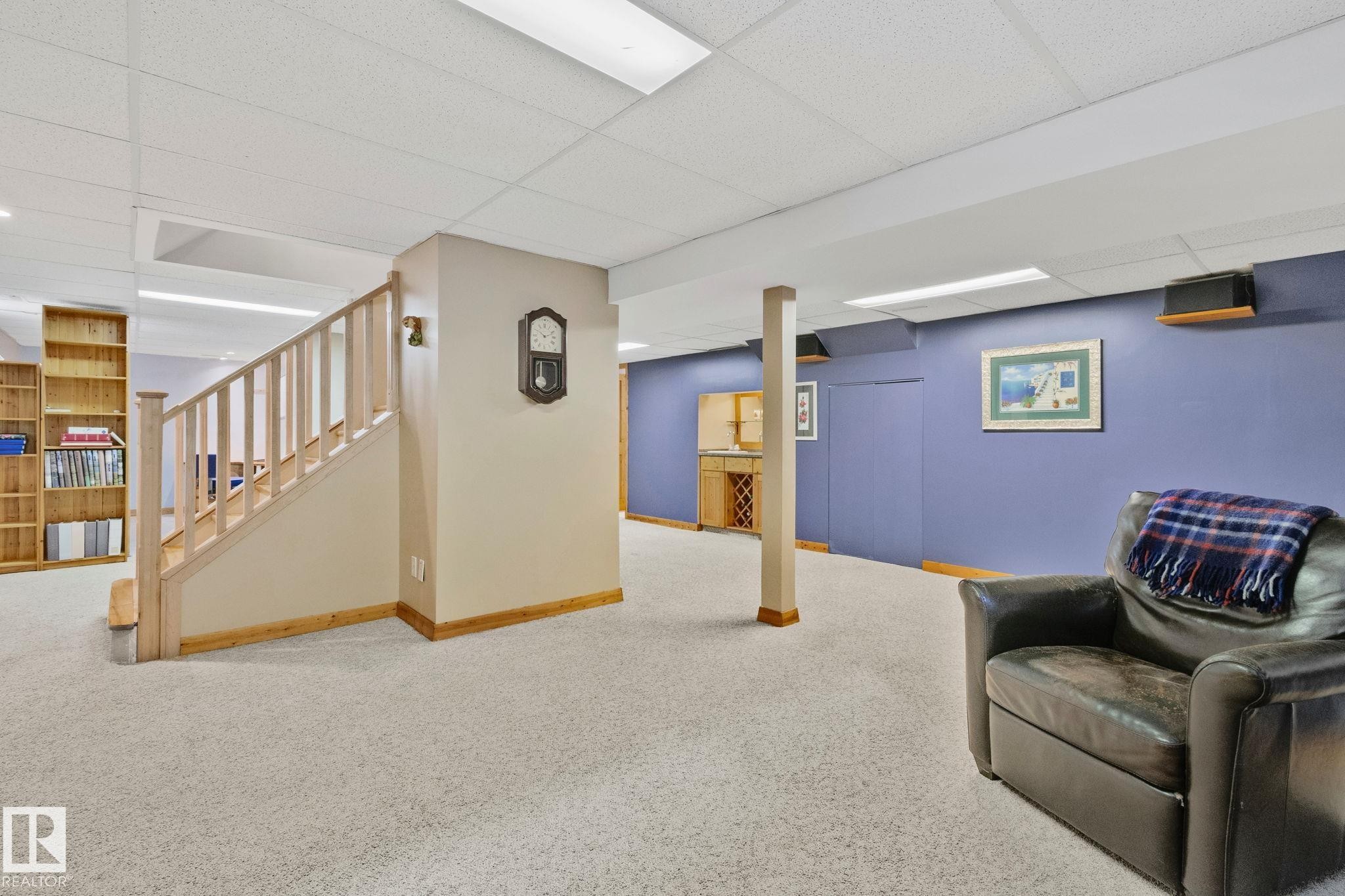Finished lower level featuring light-colored carpeting, a natural wood staircase with balusters, built-in shelving, a recessed lighting system, and a built-in bar area - 7306 21 Avenue Nw, Edmonton, AB - Indoor Photo Showing Basement