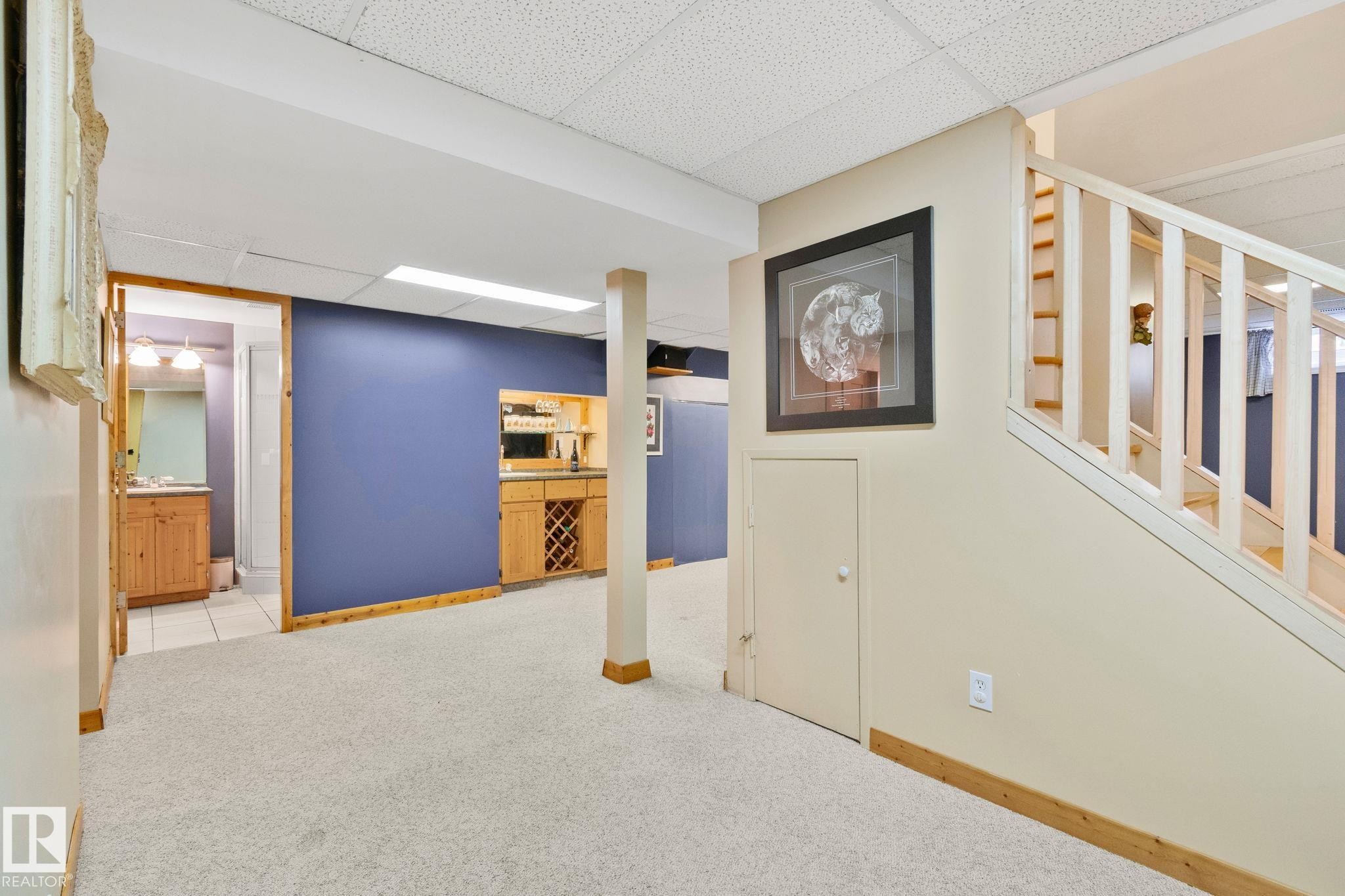 Expansive carpeted area featuring a built-in wet bar with wood cabinetry and an integrated wine rack - 7306 21 Avenue Nw, Edmonton, AB - Indoor