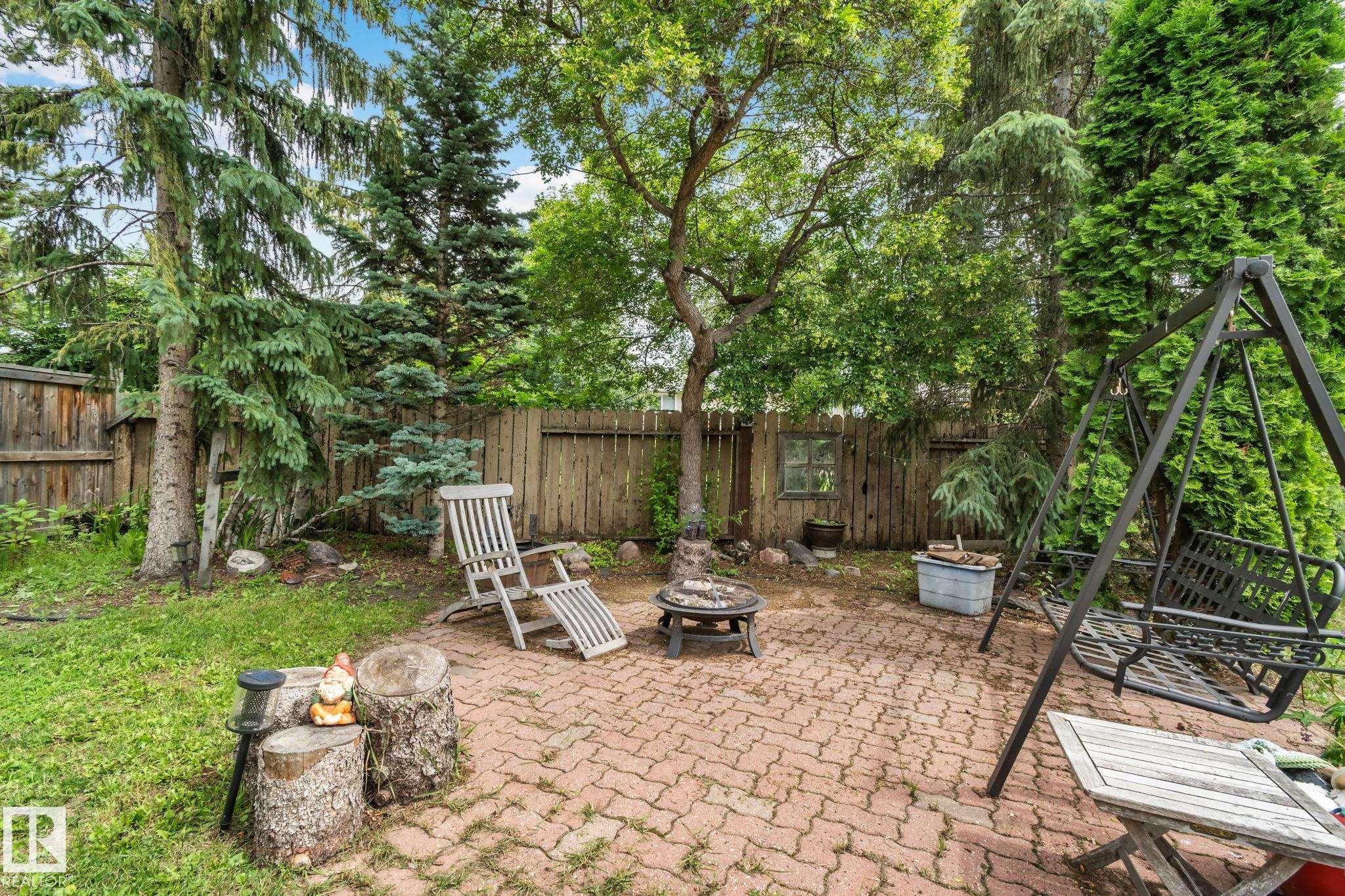 Paved brick patio with a central fire pit feature, surrounded by mature trees and a wood privacy fence - 7306 21 Avenue Nw, Edmonton, AB - Outdoor