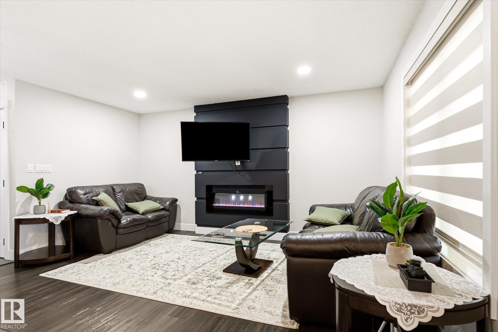 Living area featuring dark wood-finish flooring, recessed lighting, and a modern wall-mounted electric fireplace - 4317 152 Avenue Nw, Edmonton, AB - Indoor With Fireplace