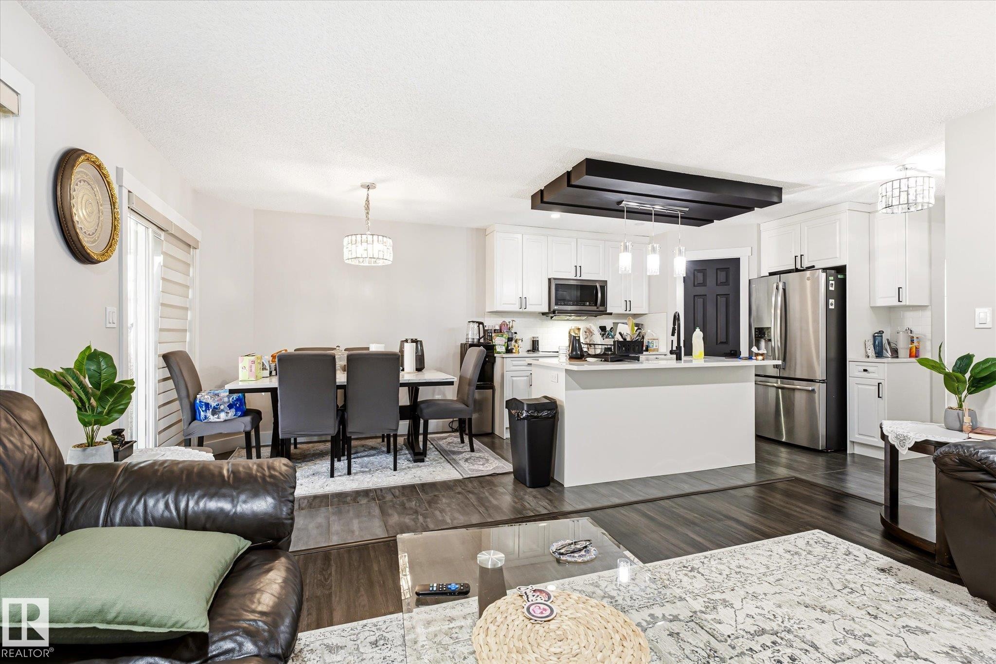 Open-concept living space featuring wood-finish flooring, a white kitchen with stainless steel appliances, a center island with pendant lighting, and a dining area with a chandelier - 4317 152 Avenue Nw, Edmonton, AB - Indoor