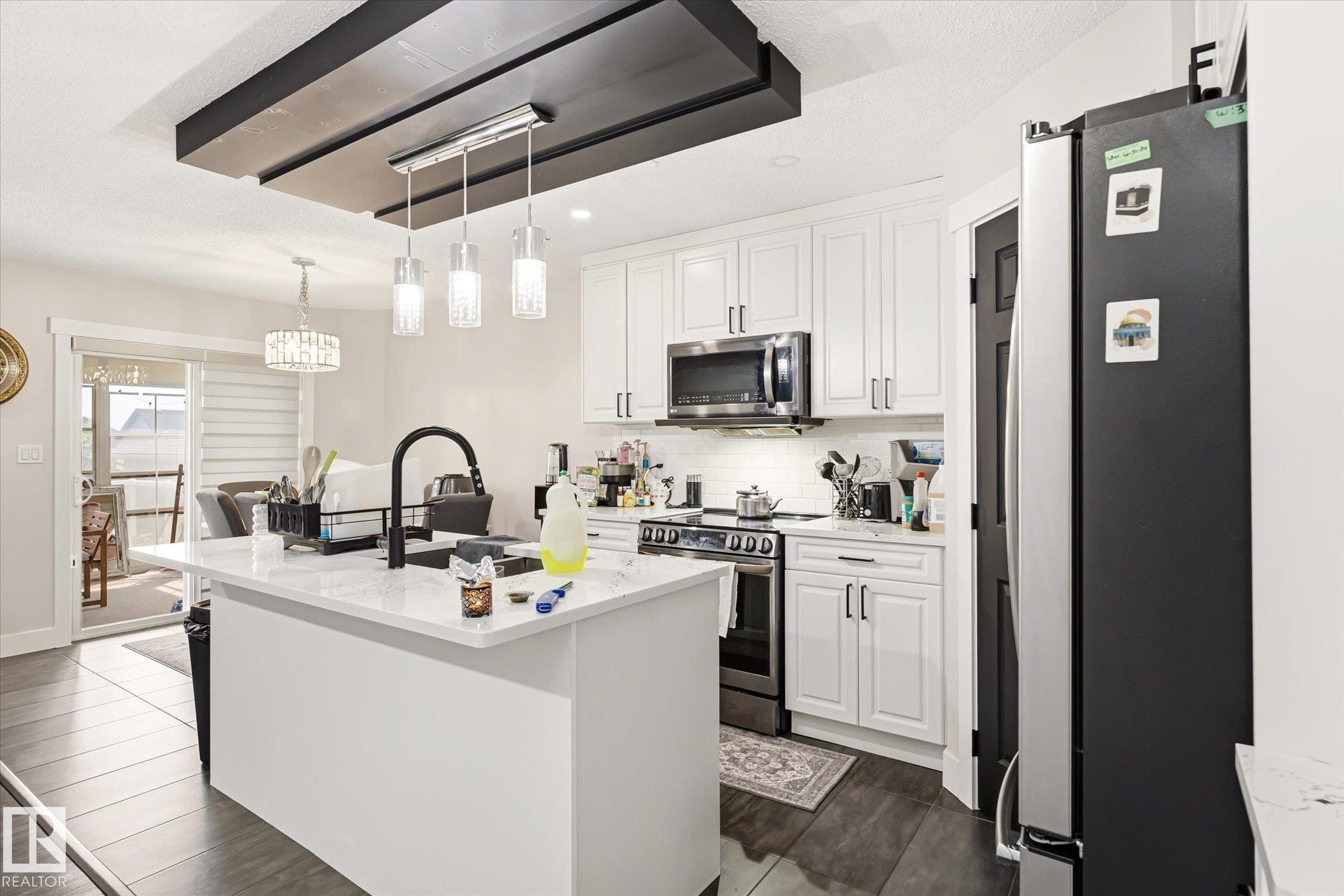 Bright kitchen featuring white shaker cabinetry, stainless steel appliances, a center island with a black faucet, and wood-finish flooring - 4317 152 Avenue Nw, Edmonton, AB - Indoor Photo Showing Kitchen With Upgraded Kitchen