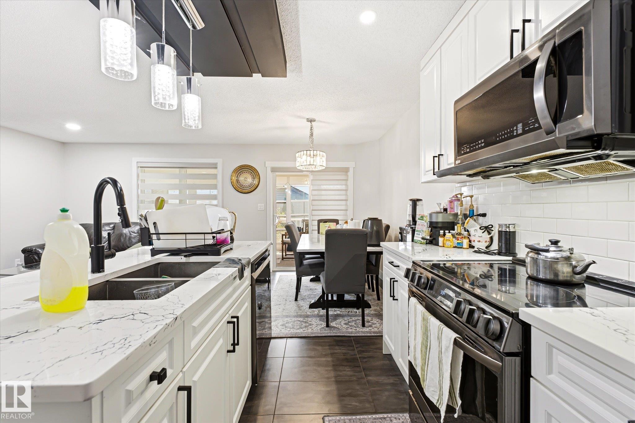 Modern kitchen featuring white cabinetry, stone-finish countertops, and stainless steel appliances - 4317 152 Avenue Nw, Edmonton, AB - Indoor Photo Showing Kitchen With Double Sink With Upgraded Kitchen