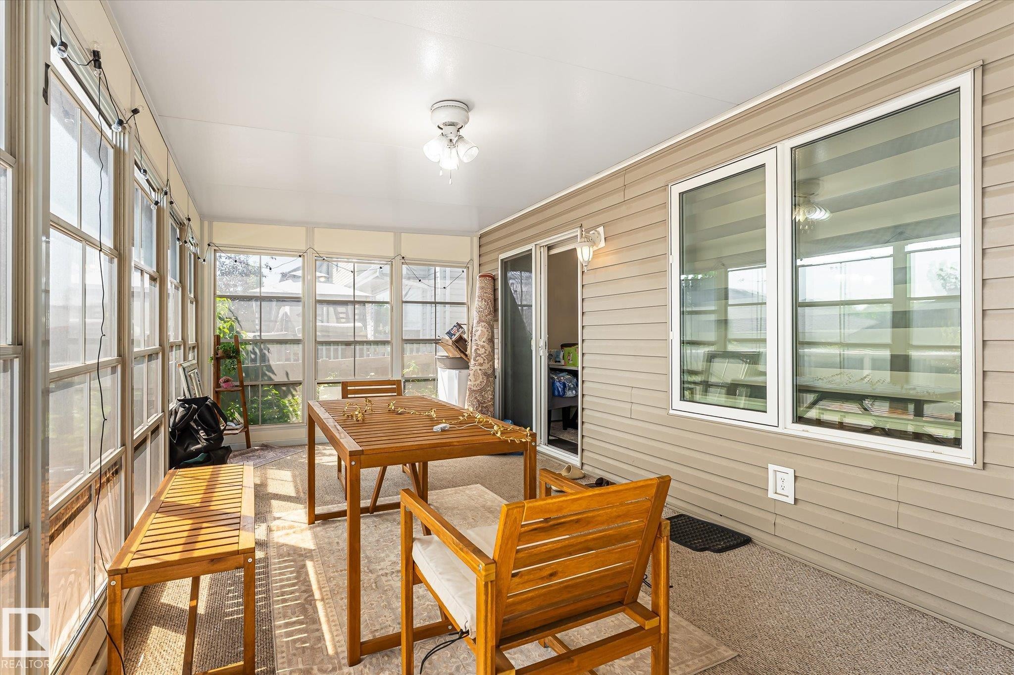 Enclosed sunroom featuring multiple large windows, wall-to-wall carpeting, a ceiling-mounted light fixture, and a sliding glass door - 4317 152 Avenue Nw, Edmonton, AB - Indoor Photo Showing Other Room