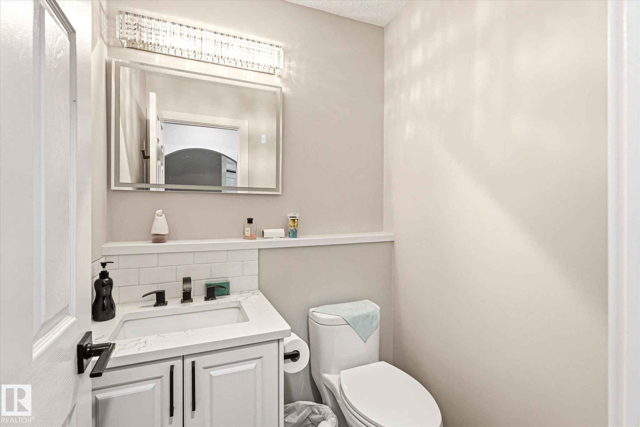 Bathroom featuring a white vanity with a quartz-finish countertop, matte black faucet, and subway tile backsplash - 4317 152 Avenue Nw, Edmonton, AB - Indoor Photo Showing Bathroom