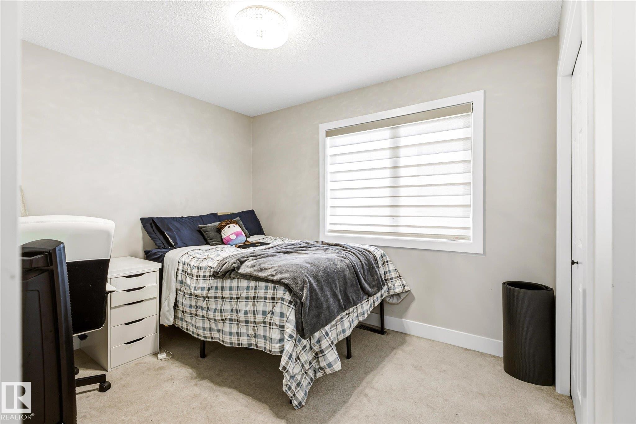 Carpeted room featuring a window with integrated blinds, a white trim package, and a flush-mount ceiling light fixture - 4317 152 Avenue Nw, Edmonton, AB - Indoor Photo Showing Bedroom
